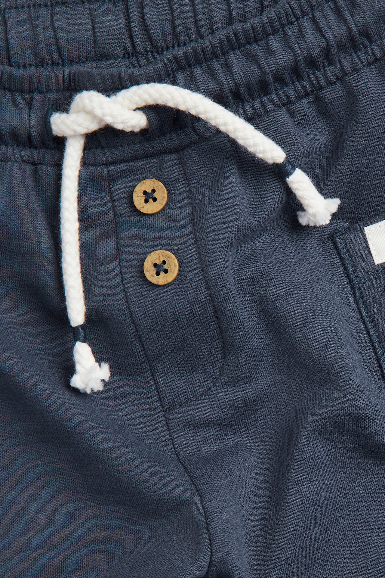 Nærbilde av mørkeblå bomullsshorts med elastisk midje, hvit snøring og to dekorative treknapper.