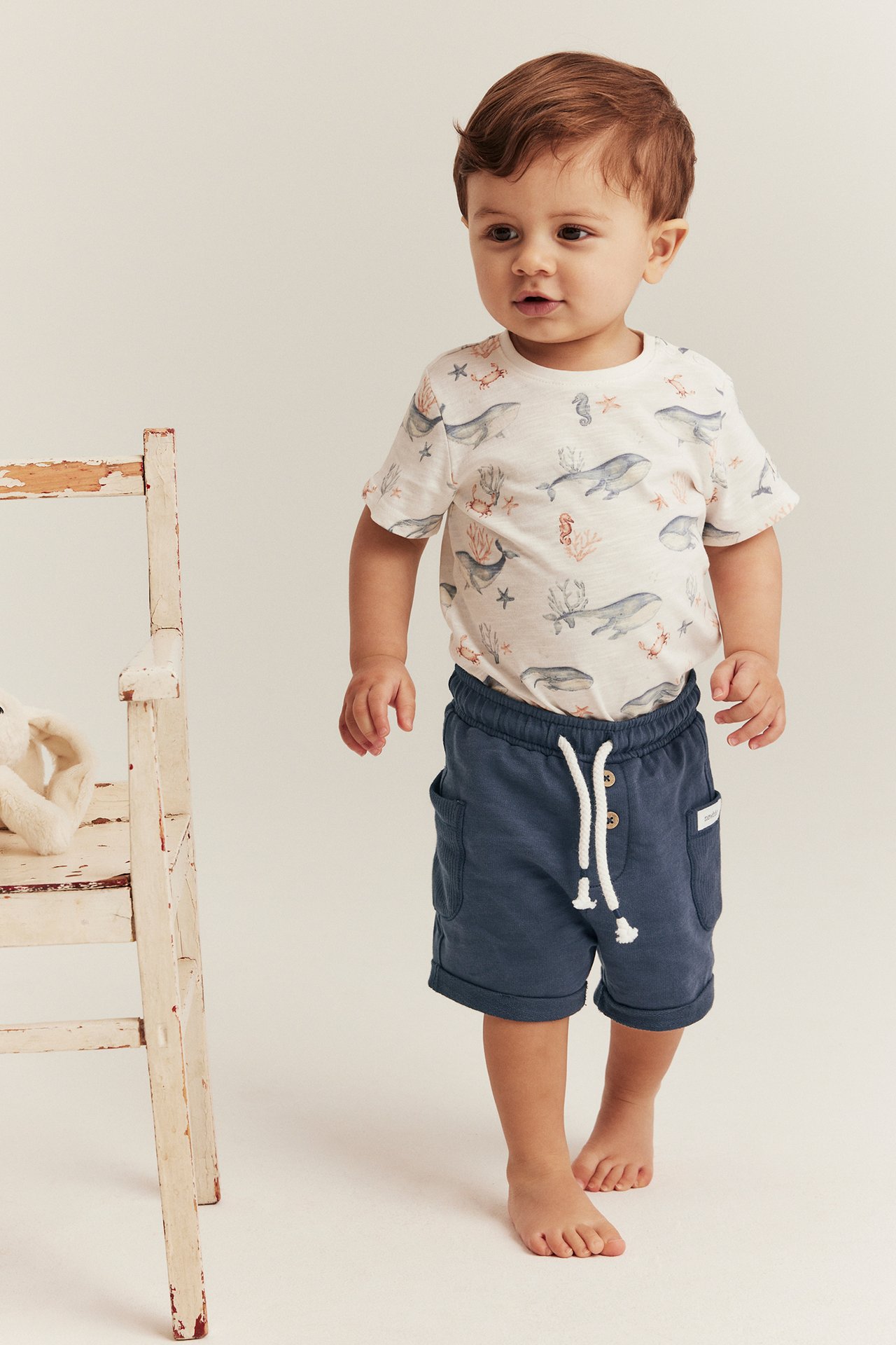 Baby forfra: mørkeblå slub-jersey shorts med hvit snøring og hvit mønstret t-skjorte.