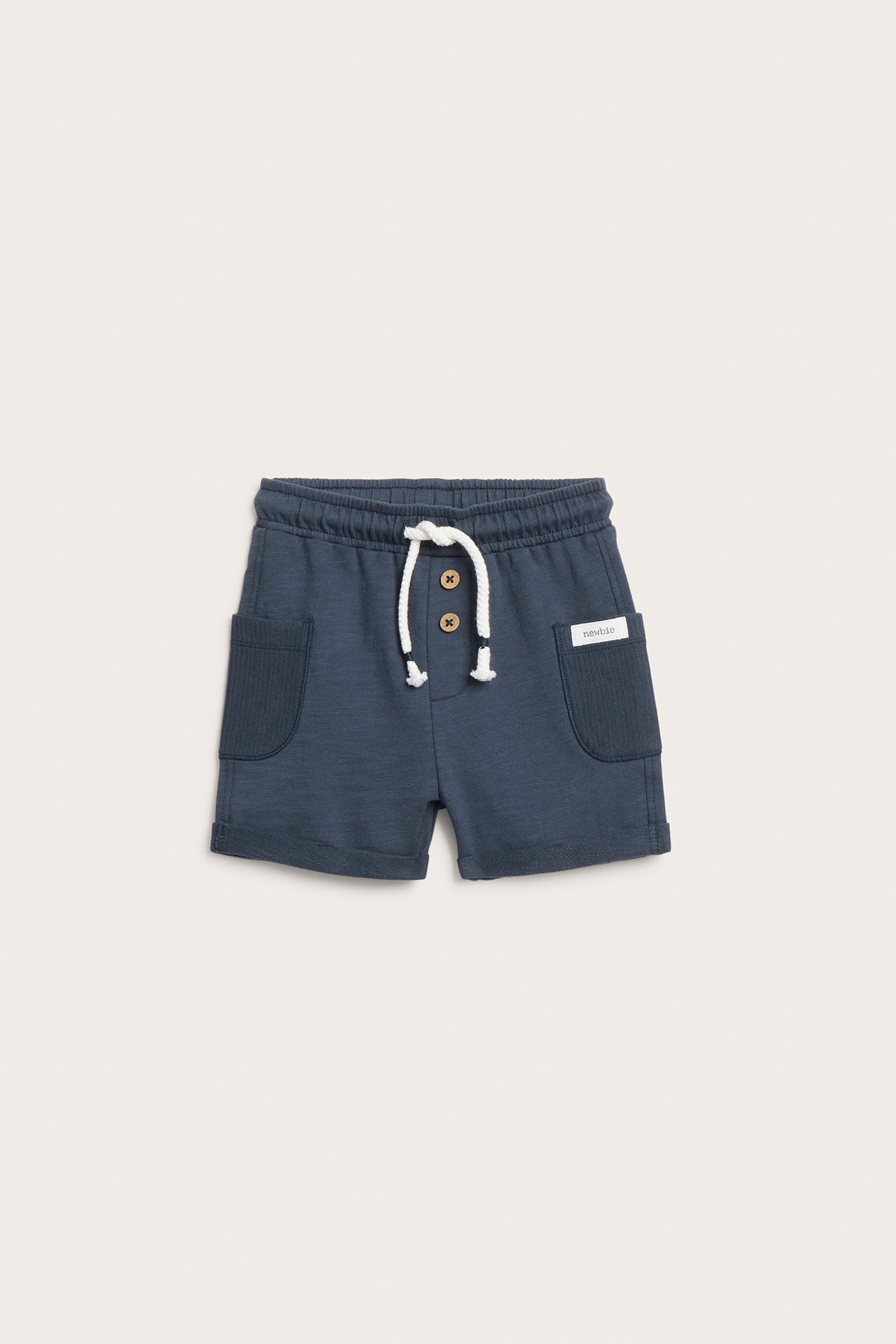 Frontvisning: Mørkeblå barneshorts, ribbelommer, oppbrettede ben, dekorative knapper, hvit snøring.