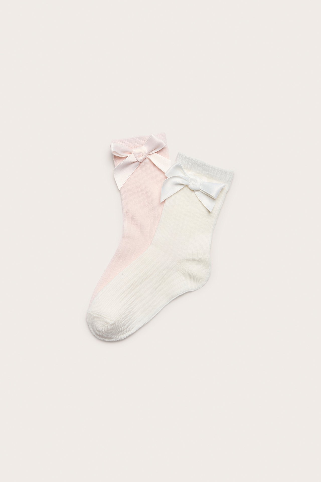 Uppifrån sett, två par ribbade barnstrumpor: offwhite och ljusrosa, båda med en satinrosett.