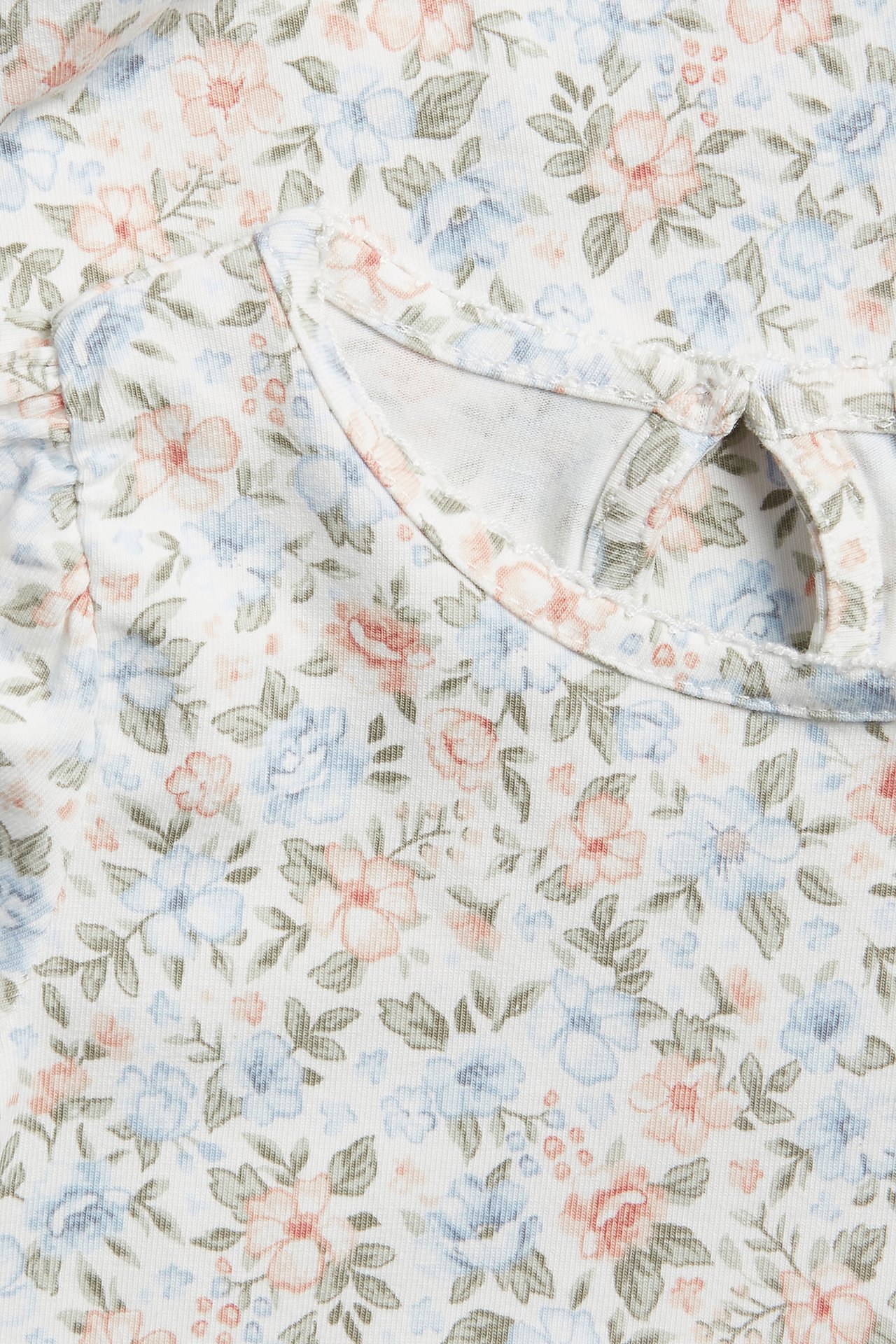 Nærbilde av en offwhite babybody med småblomstret mønster, korte puffermer og nøkkelhullsåpning bak.