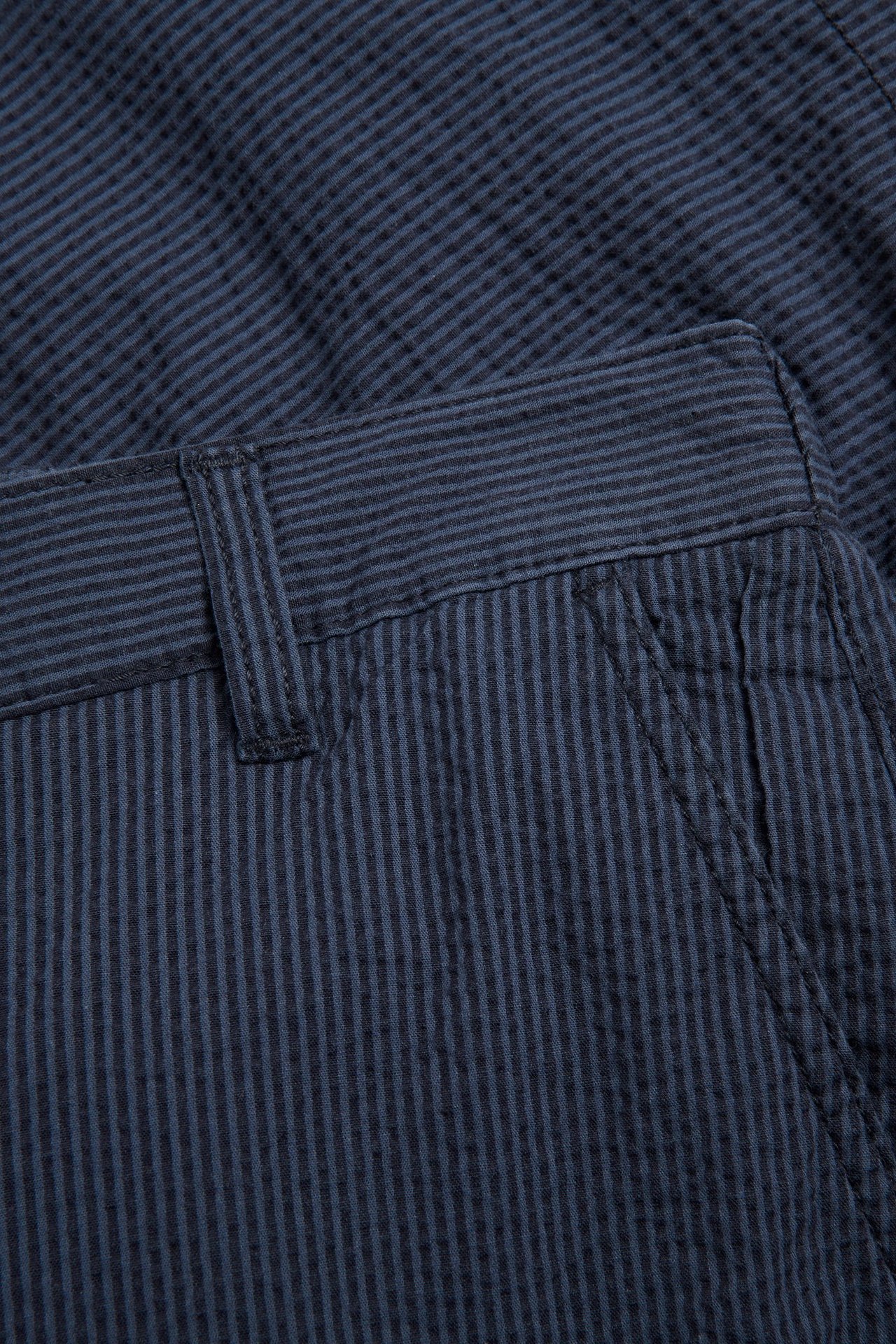 Zbliżenie na niebieskie, pasiasty szorty z seersuckeru z paskiem, szlufką i kieszenią.