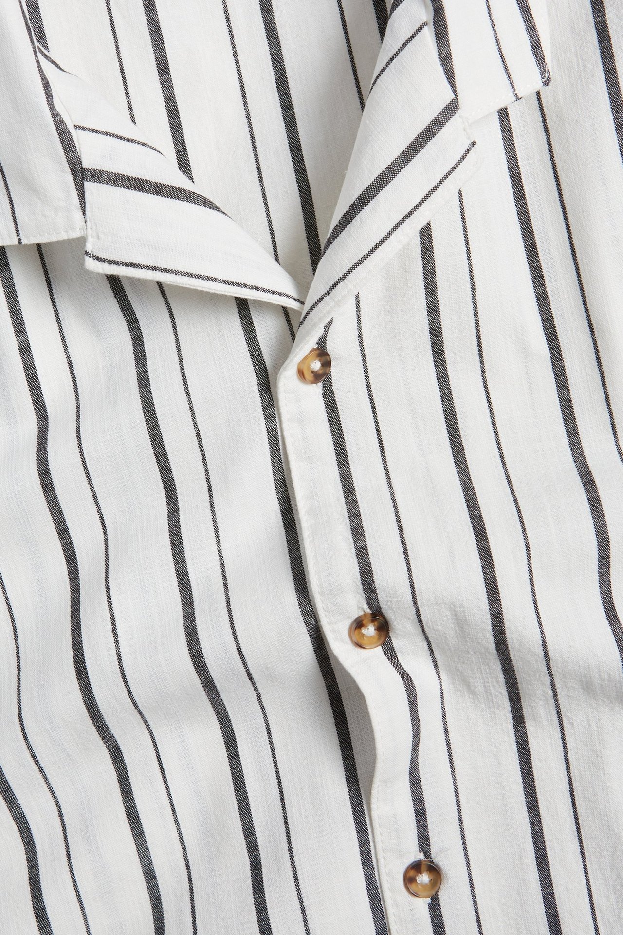 Zbliżenie białej bawełnianej koszuli z krótkim rękawem, z czarnymi paskami i brązowymi guzikami.