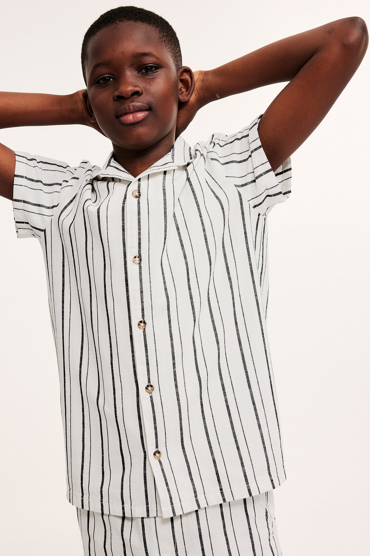 Widok z przodu dziecka w białej, krótko rękawowej koszuli w czarne paski i pasujących szortach.