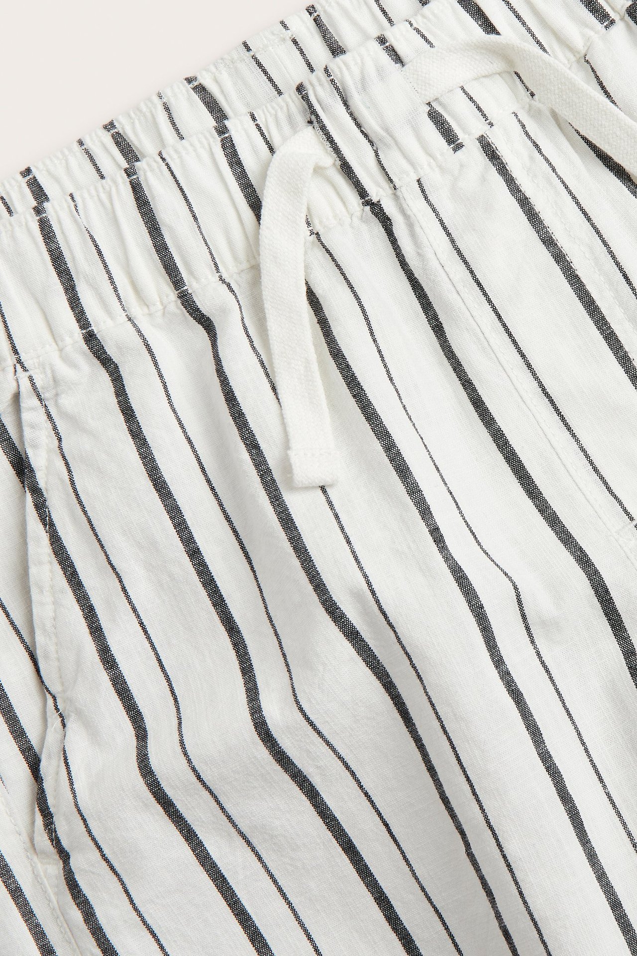 Zbliżenie białych bawełnianych szortów w czarne paski, z elastyczną talią i białym sznurkiem.