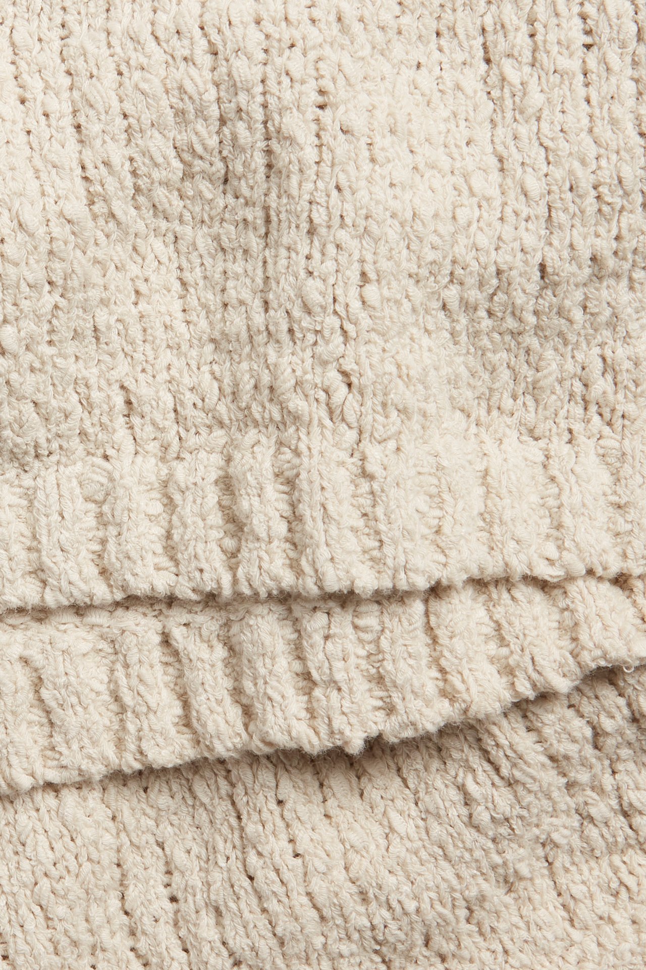 Nærbilde av en lys beige strikket topp med boucle-effekt, som viser dens teksturerte ensfargede stoff.