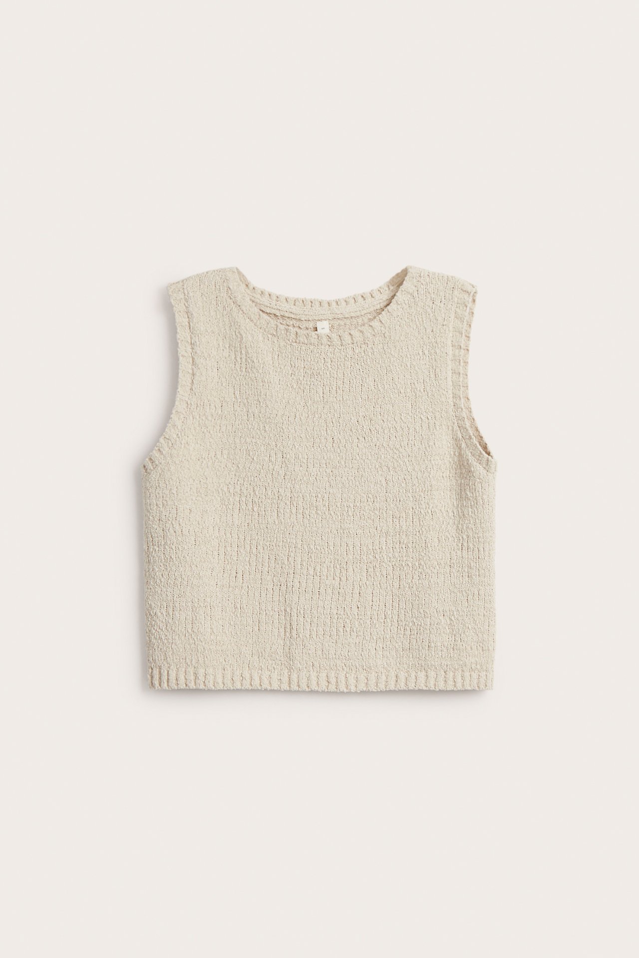 Frontvisning av en lys beige strikket ermeløs topp med boucle-effekt og ribbet kant.