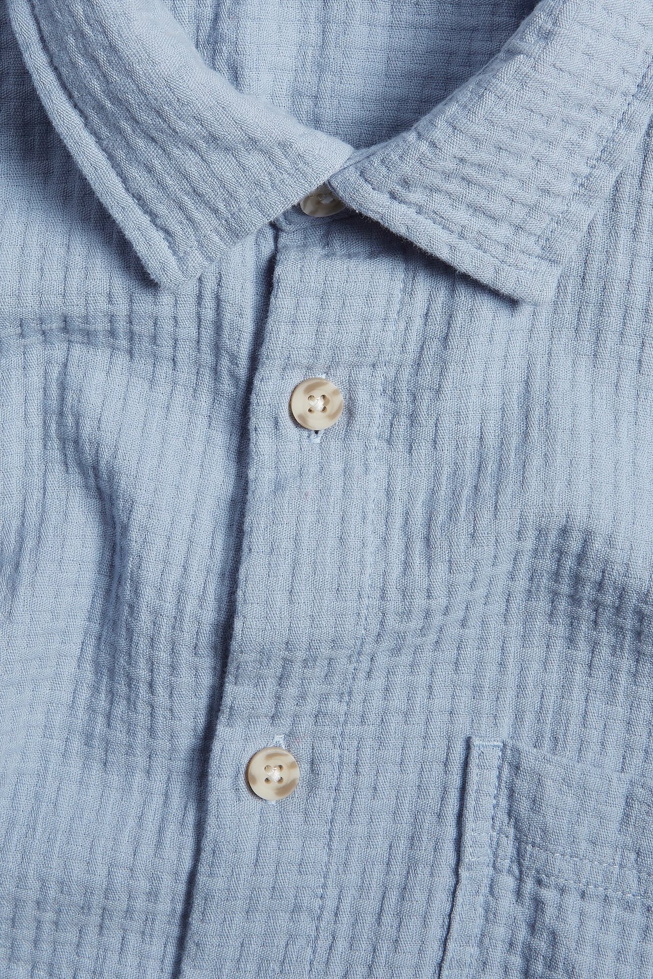 Zbliżenie jasnoniebieskiej koszuli z krótkim rękawem, z teksturowanej bawełny, z kołnierzykiem i guzikami.