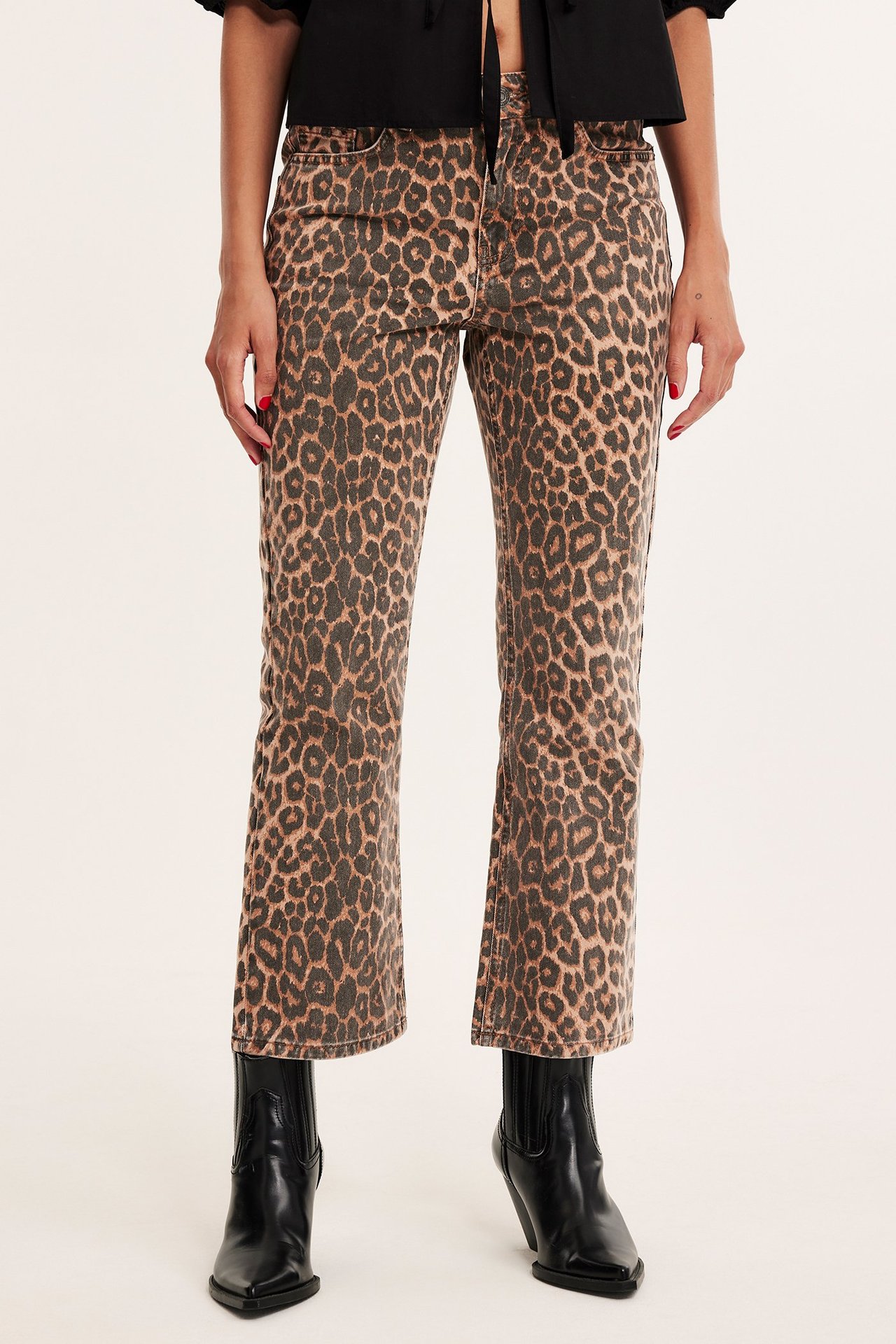 Frontvy av en kvinna i beigefärgade leopardmönstrade cropped flare jeans, svart topp och svarta stövlar.