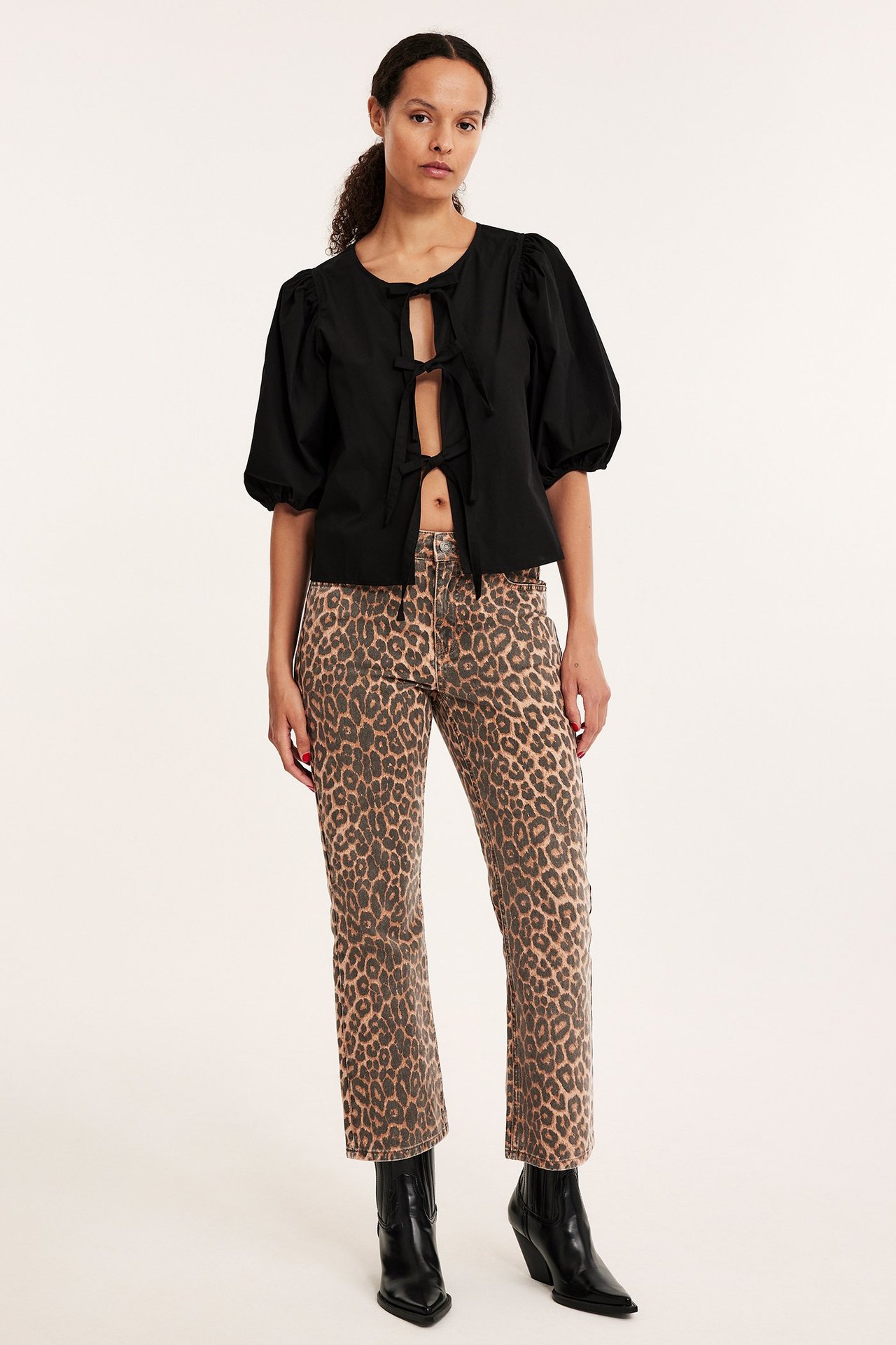 Framifrån av en kvinna i beige leopardmönstrade cropped flare jeans, svart knytblus och svarta stövlar.