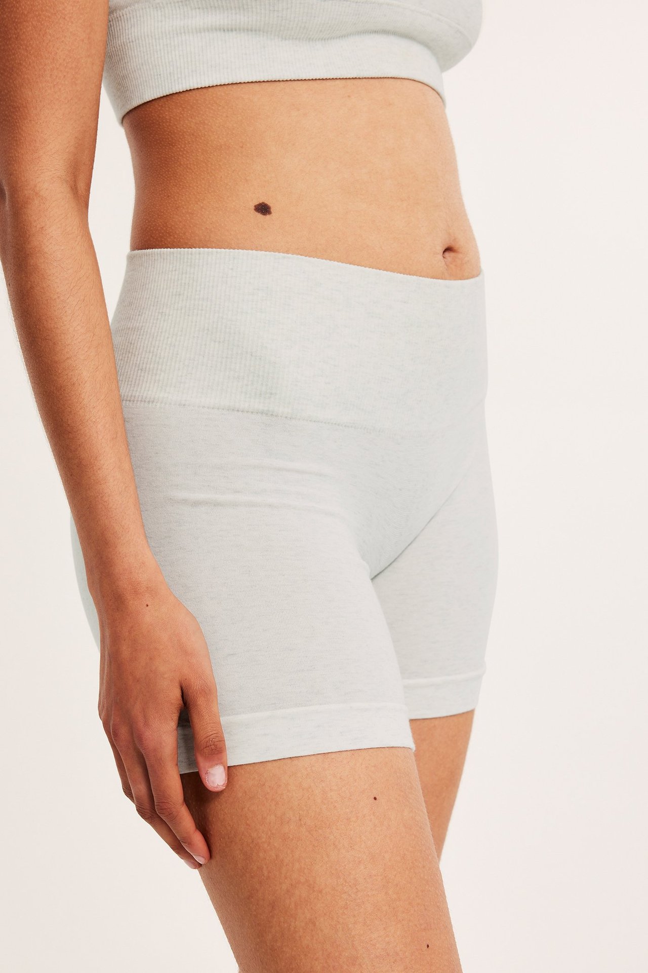 Sidovy av en kvinna i ljusgråmelerade åtsittande shortstrosor med ribbad midja och matchande BH-topp.