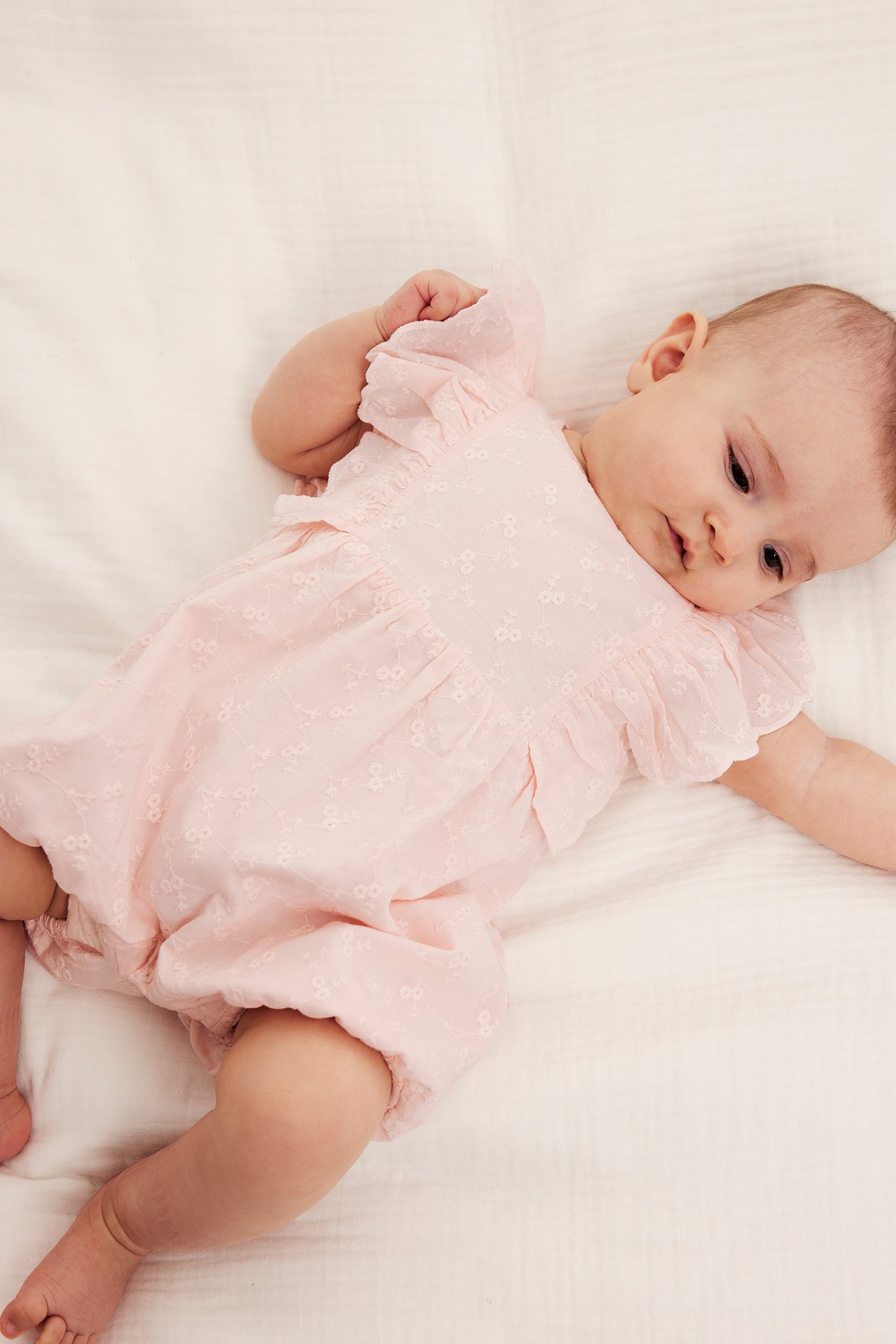 Ovenfra: baby i lyserosa broderie anglaise playsuit med skulderfriller.