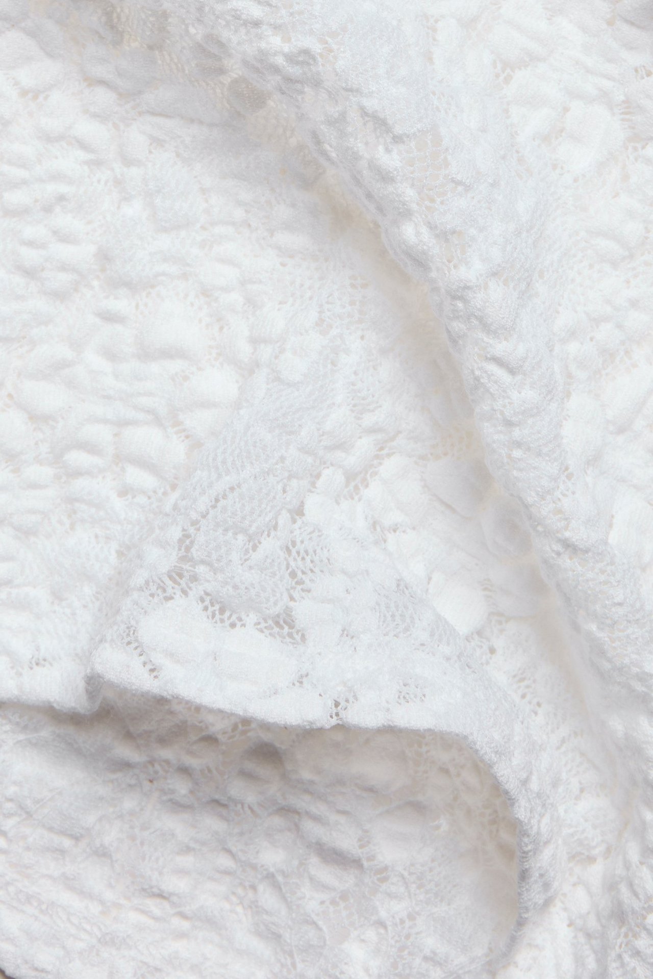 Zbliżenie białej koronki z delikatnym kwiatowym wzorem.