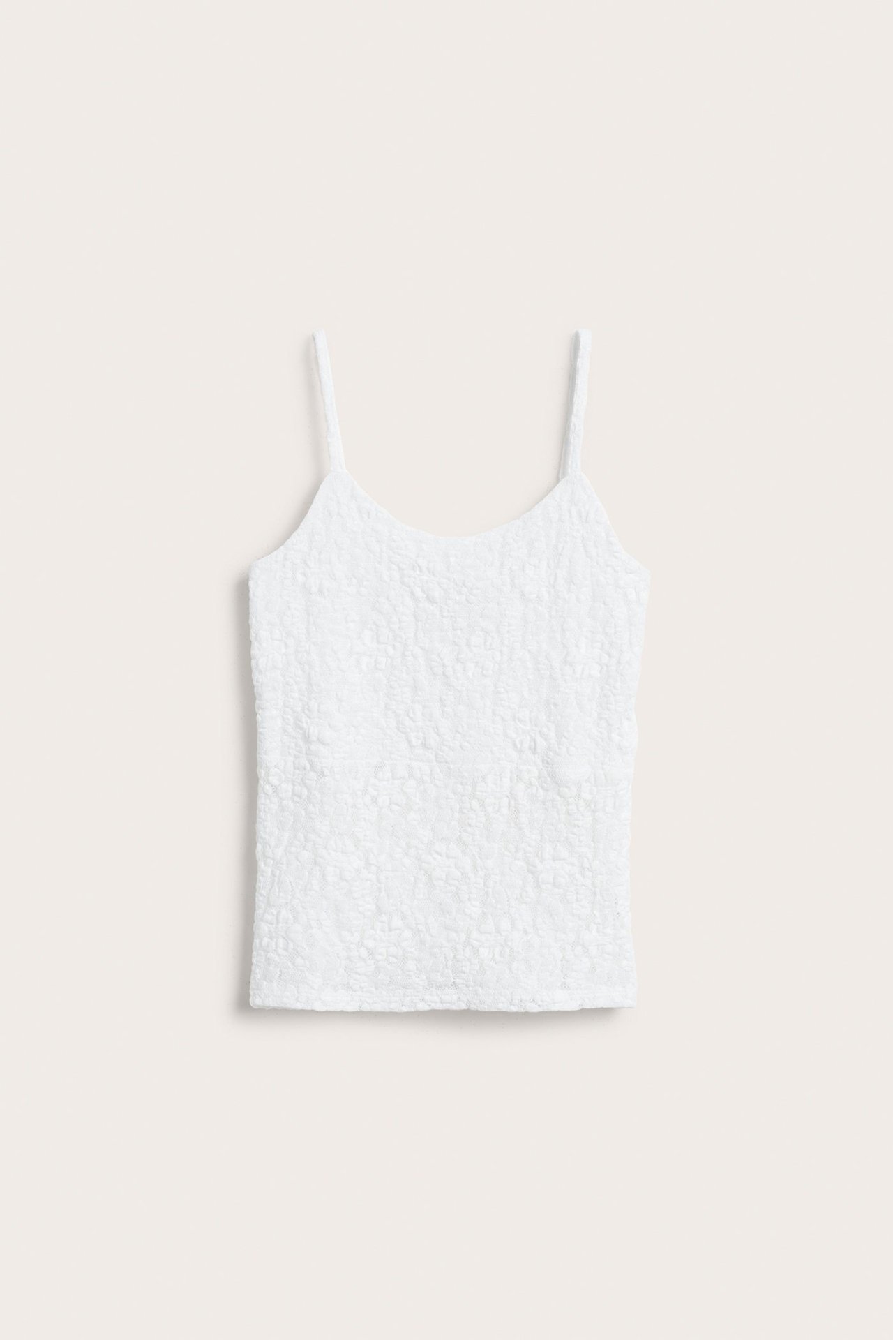 Frontvy av ett vitt spetslinne med smala axelband och texturerat mönster.