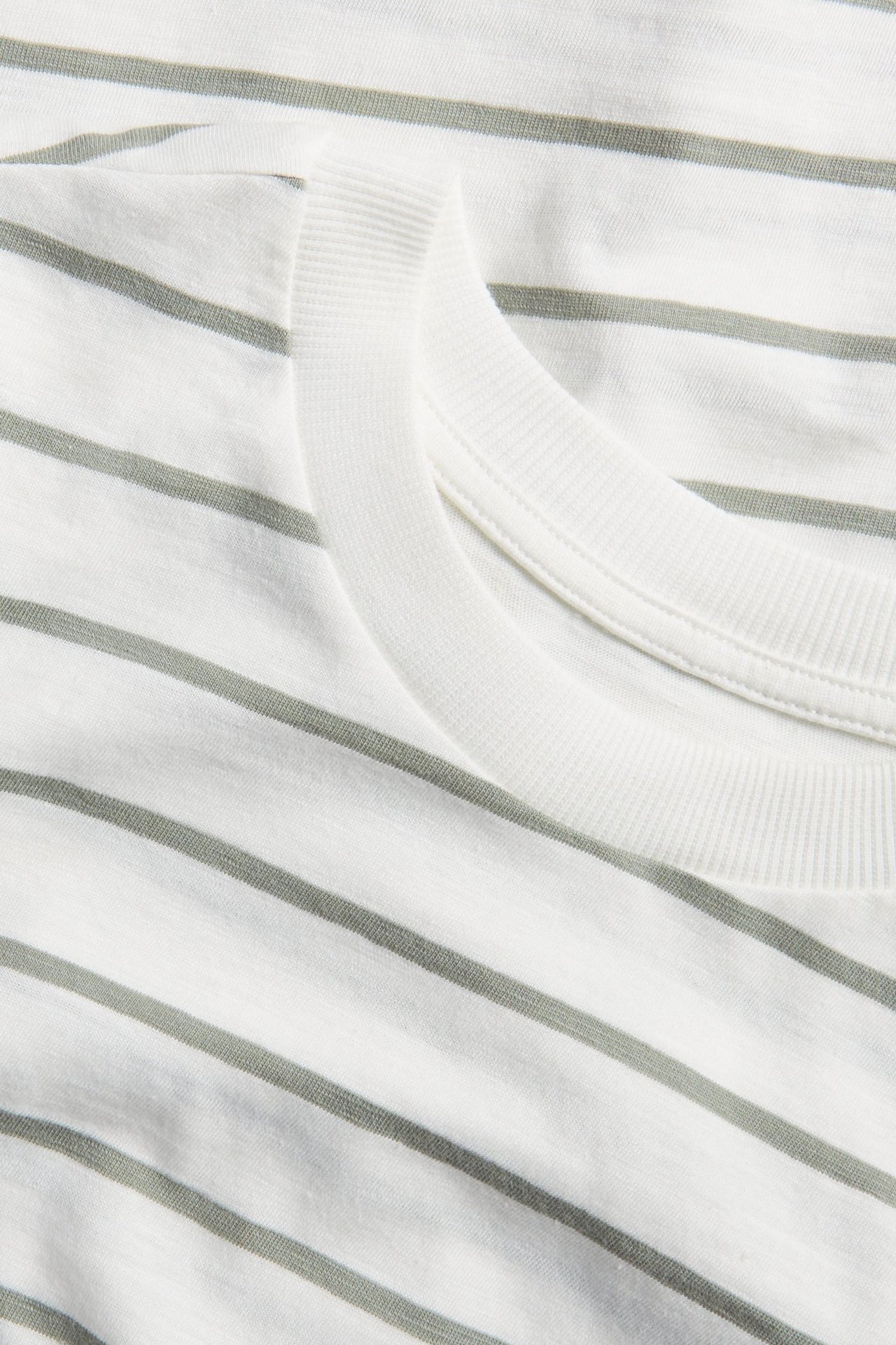 Zbliżenie białego bawełnianego t-shirtu w zielone paski z prążkowanym dekoltem.