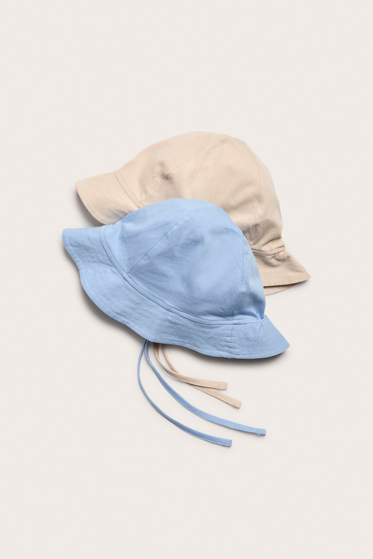 Widok z góry na jasnoniebieski bawełniany kapelusz przeciwsłoneczny z wiązaniami, na beżowym kapeluszu.