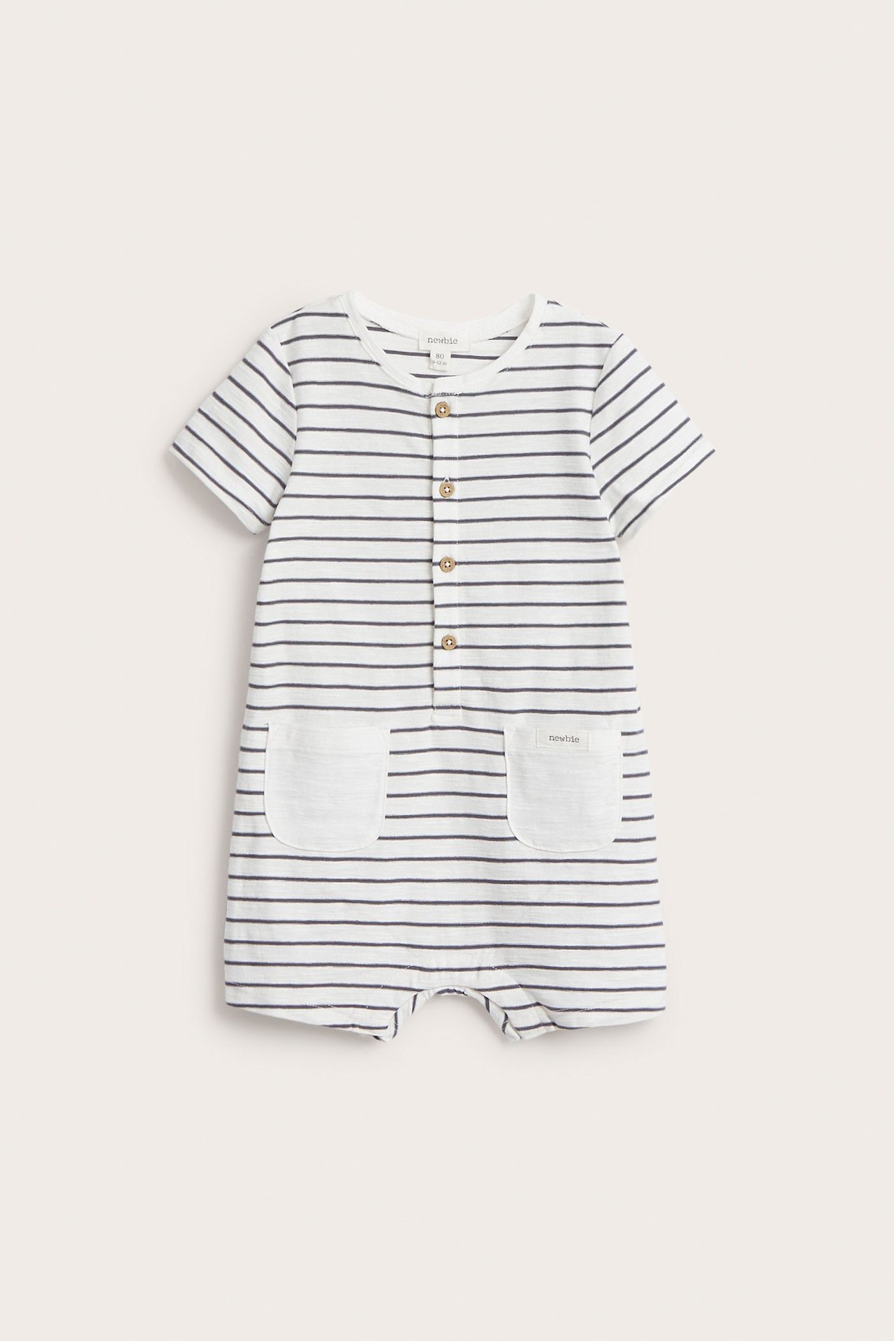 Frontvisning av en offwhite stripete babyplaysuit med korte ermer, knapper foran og to lommer.
