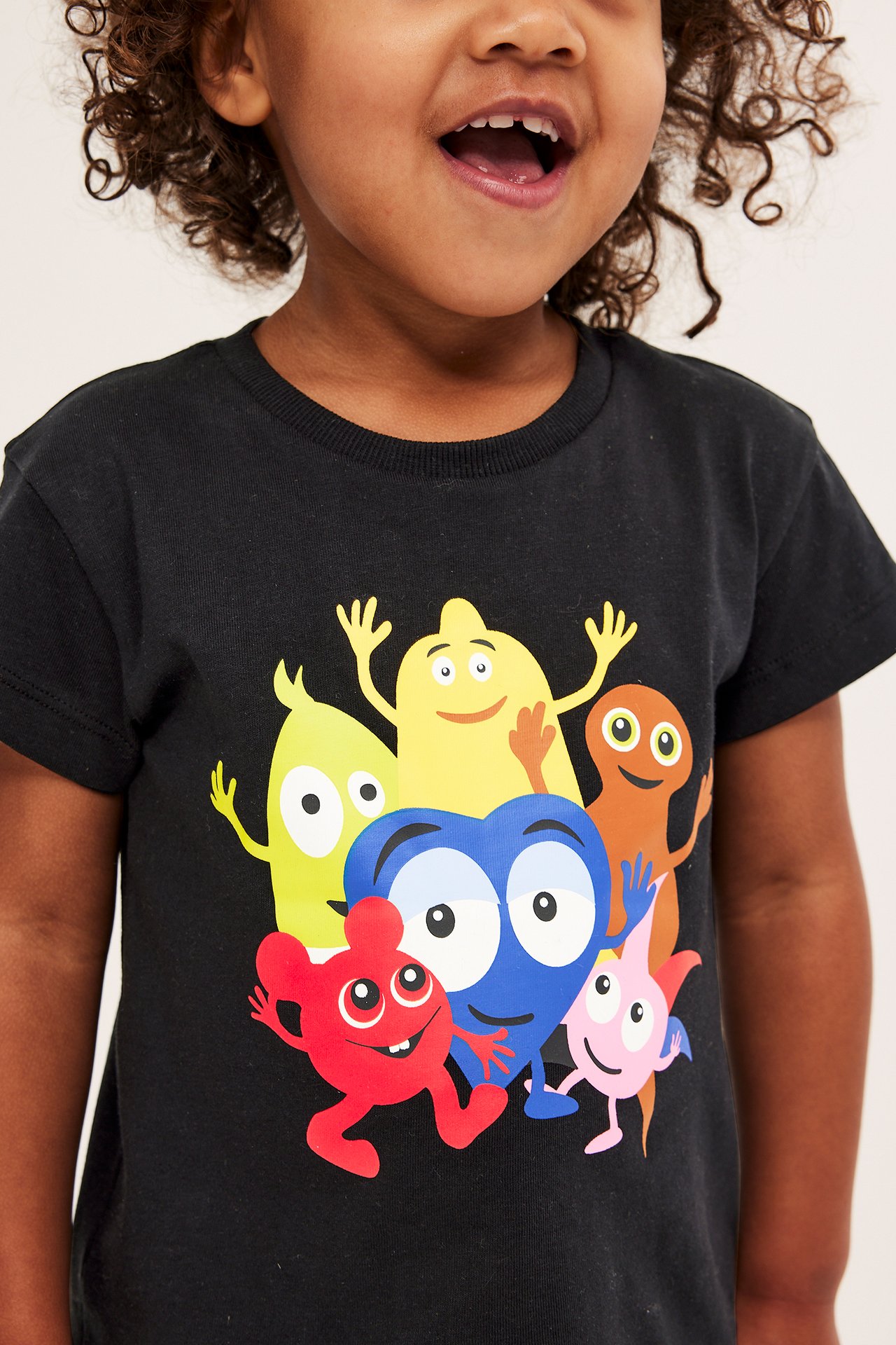 Zbliżenie z przodu na dziecko w czarnym bawełnianym T-shircie z kolorowym nadrukiem Babblarna.