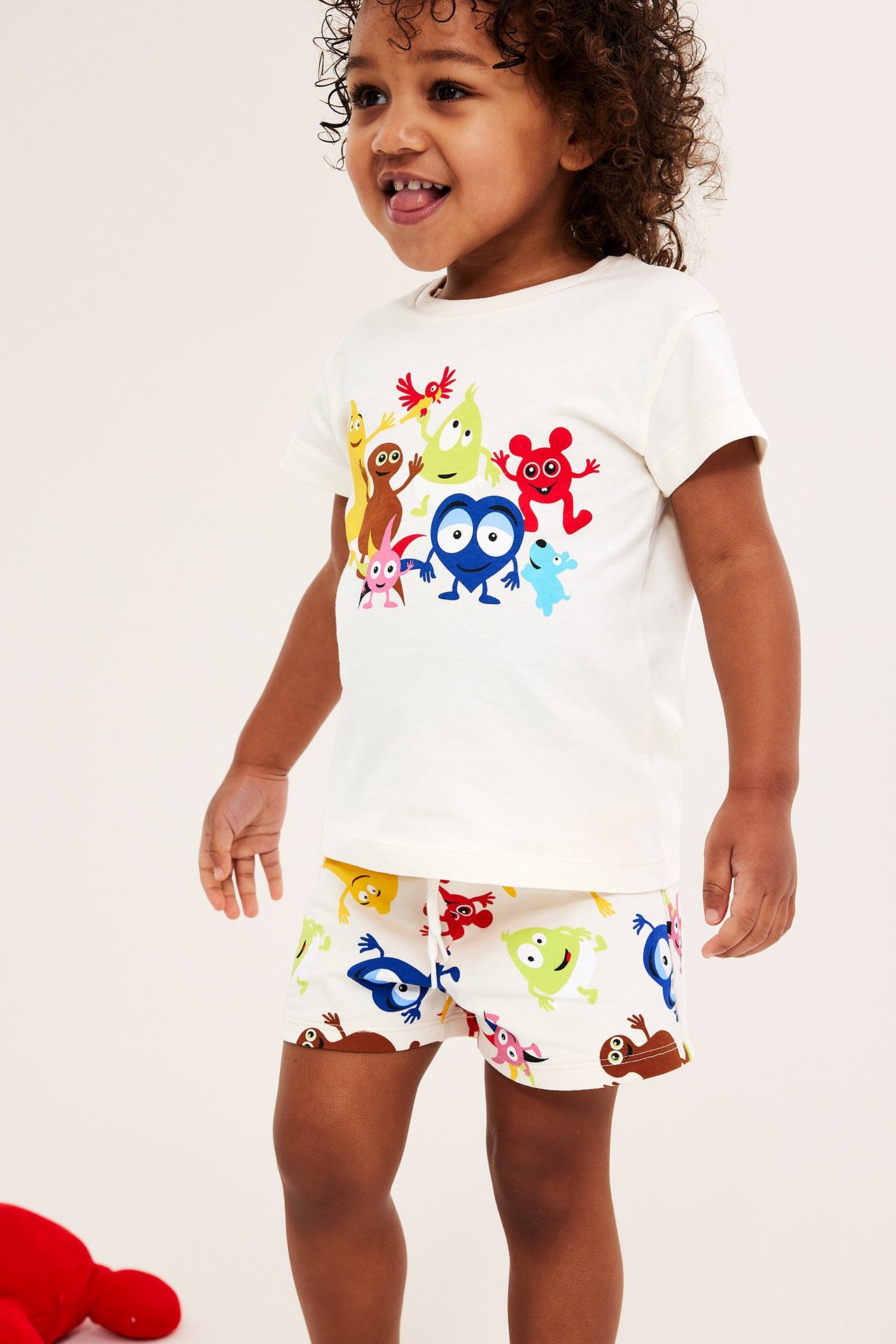 Edestäpäin: lapsi yllään luonnonvalkoiset Babblarna-kuvioiset puuvillashortsit ja yhteensopiva t-paita.