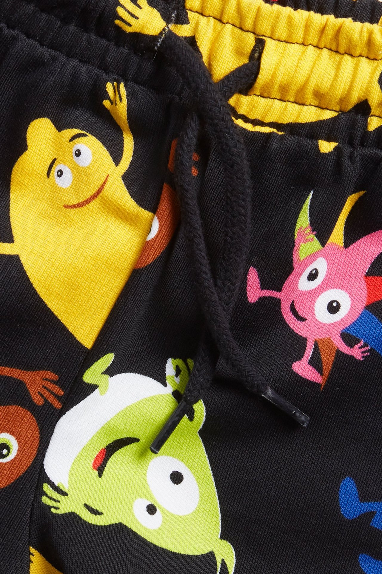 Zbliżenie na czarne bawełniane szorty dresowe z wzorem Babblarna, czarnym sznurkiem i żółtym pasem.