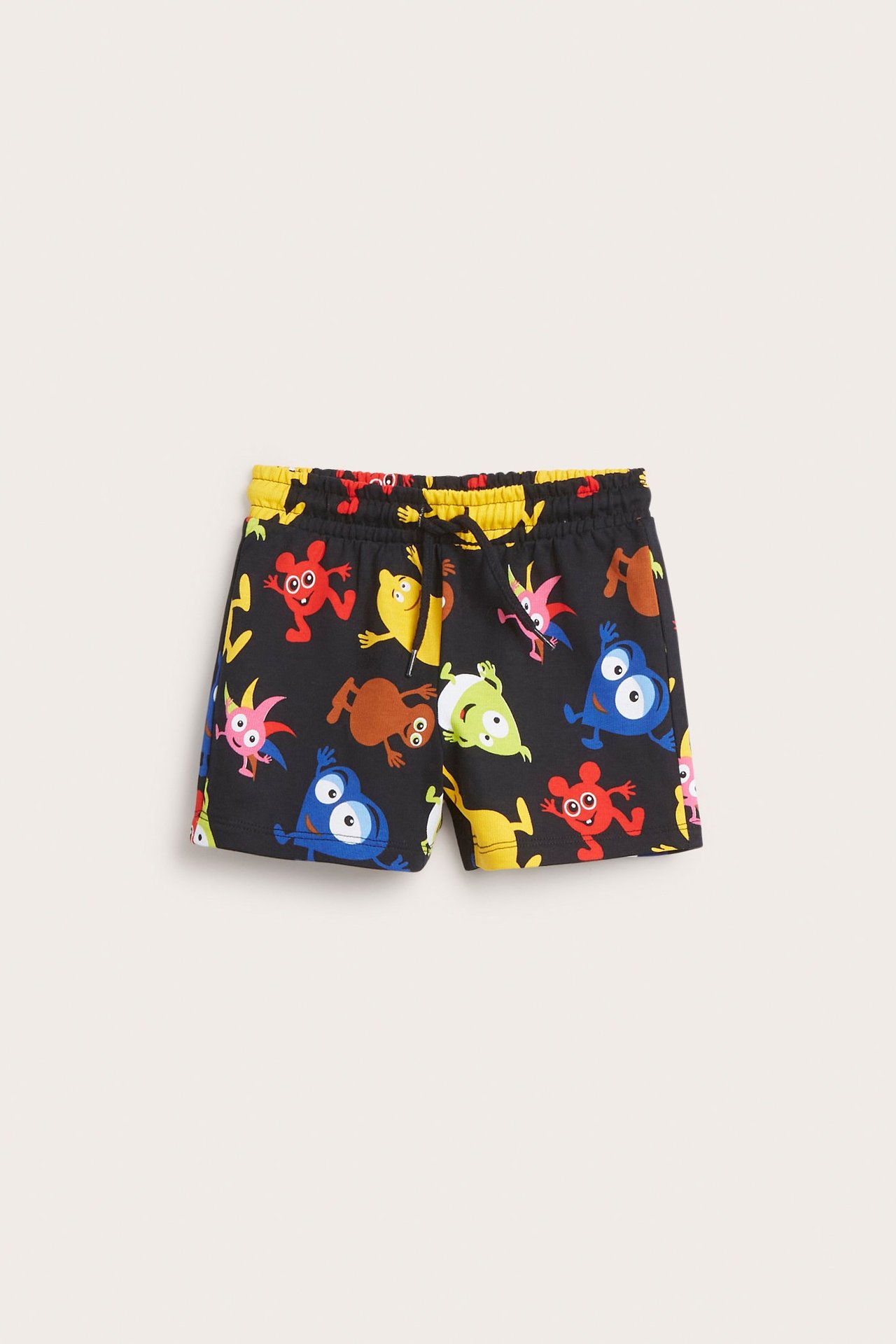 Edestä näkymä lasten mustista puuvillafroteeshortseista, joissa on värikäs Babblarna-kuvio ja keltainen kuminauhavyötärö.