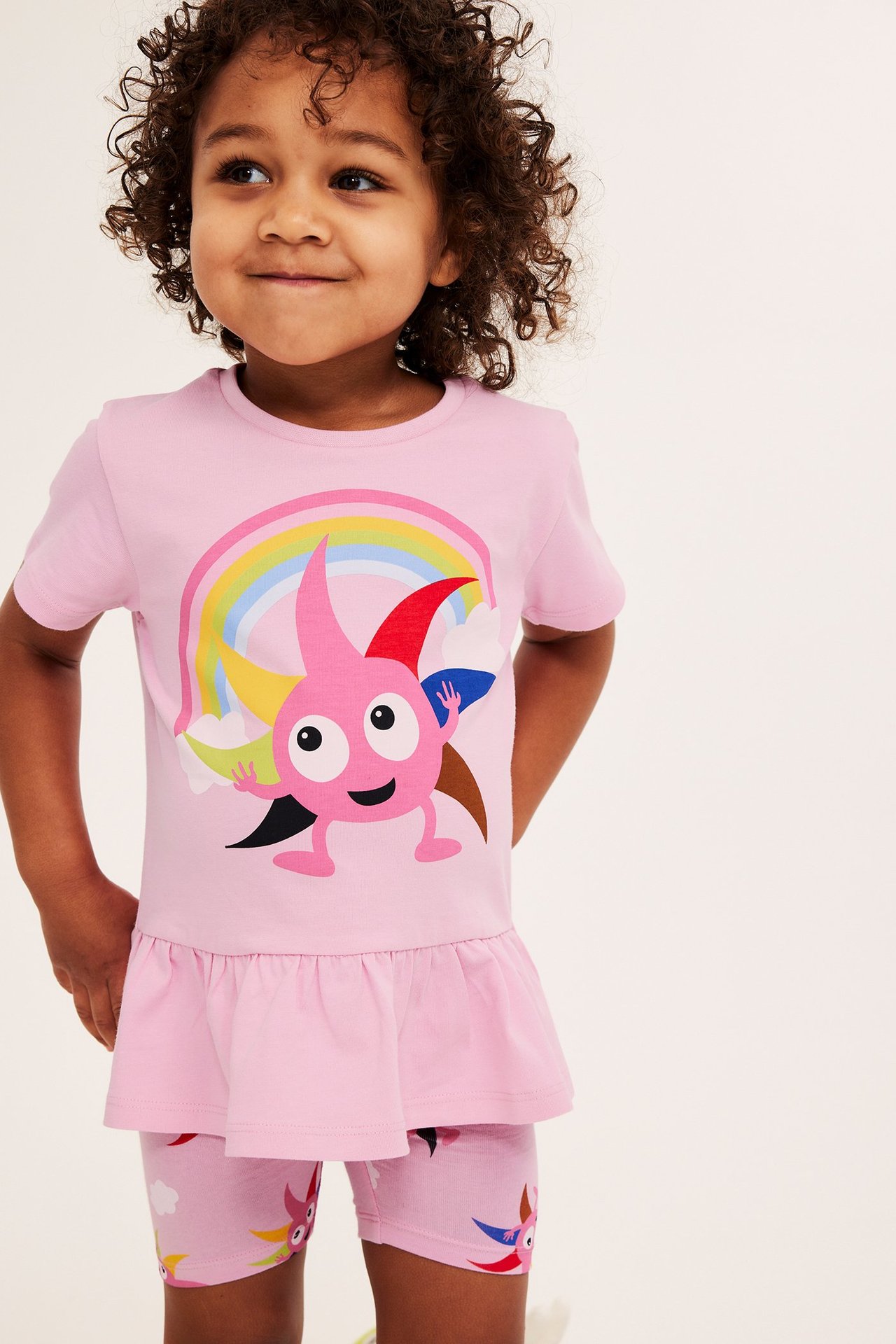 Edestä kuvattu lapsi yllään vaaleanpunaiset kuvioidut Diddi-pyöräilyhousut ja vaaleanpunainen Diddi-t-paita sateenkaarella.