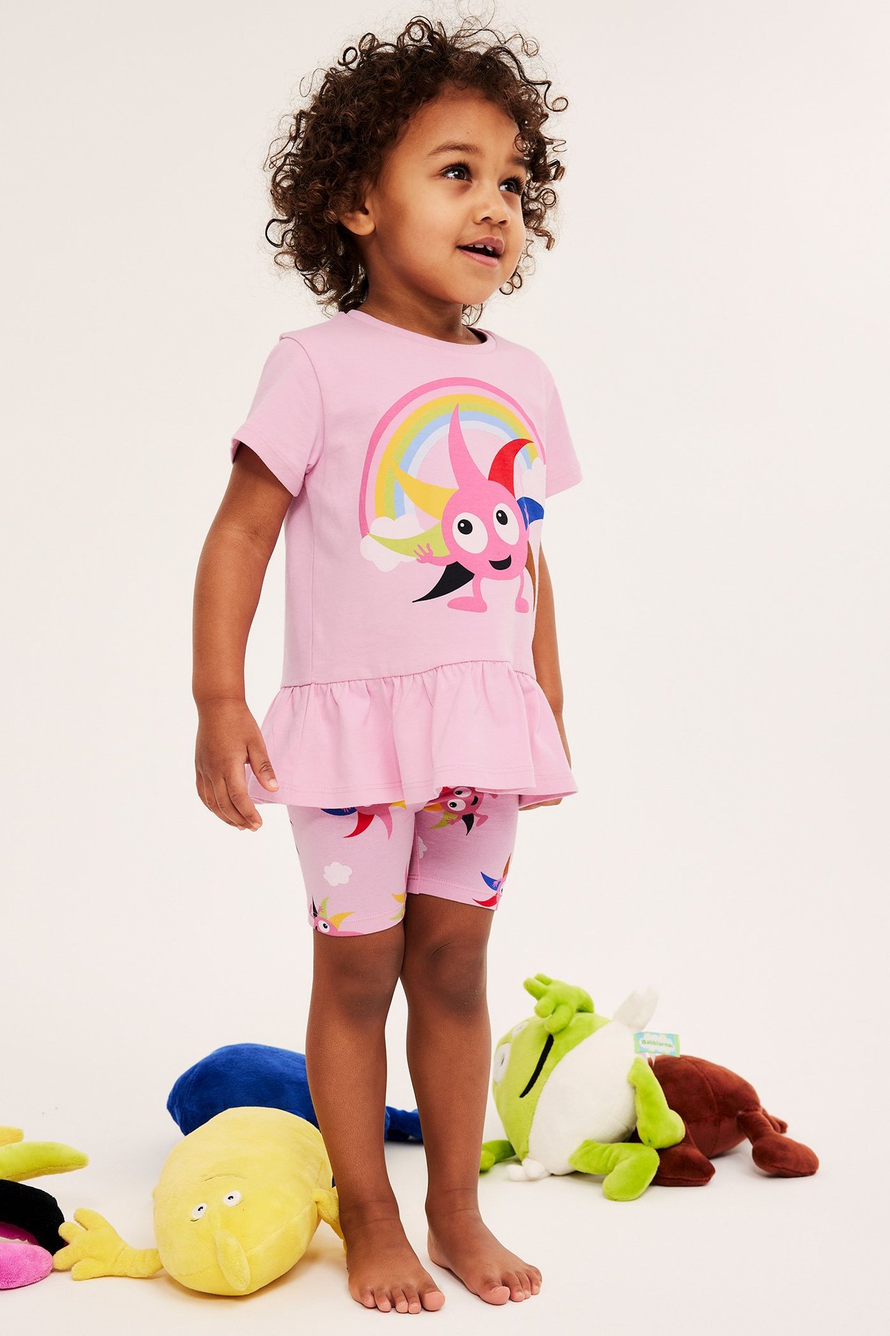 Edestäpäin lapsi yllään vaaleanpunaiset kuviolliset pyöräilyhousut ja Diddi-kuvioinen toppi.