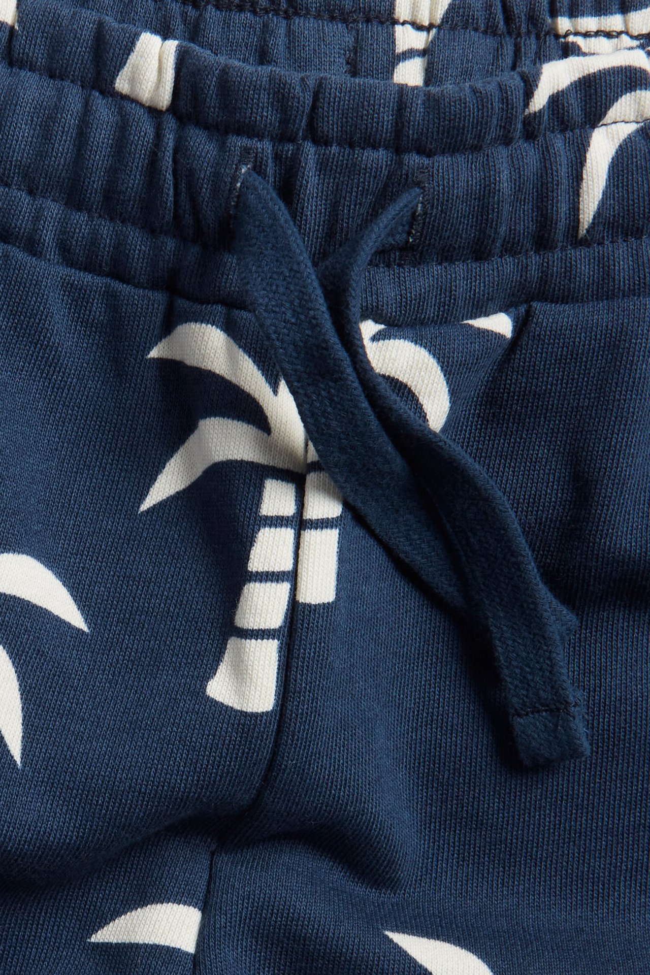Zbliżenie na granatowe bawełniane szorty dresowe dla dzieci z białym wzorem palm i sznurkiem w pasie.