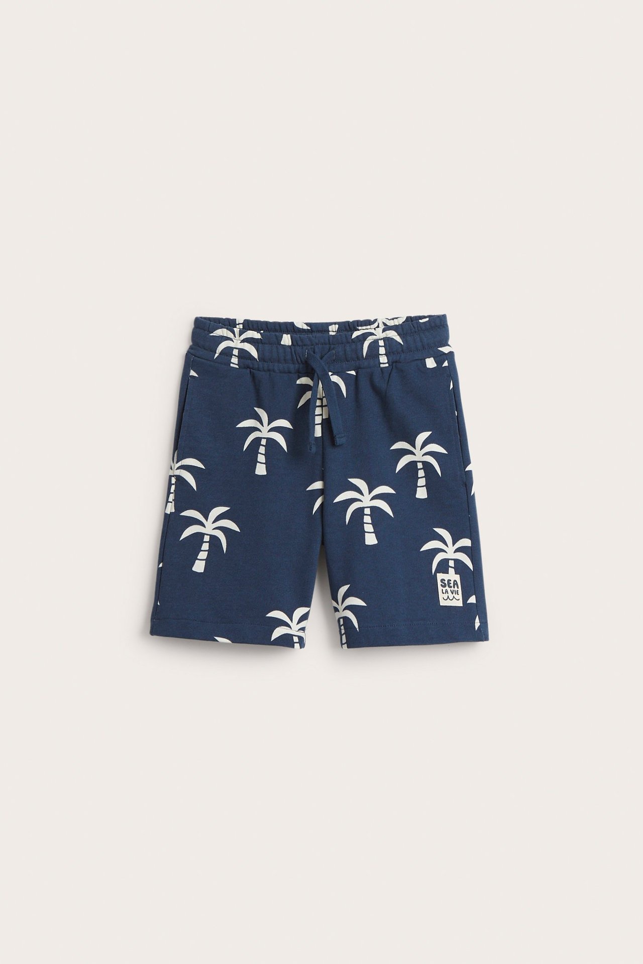 Edestä lasten tummansiniset puuvillashortsit valkoisella palmukuviolla, joustovyötärö, kiristysnyöri, taskut.