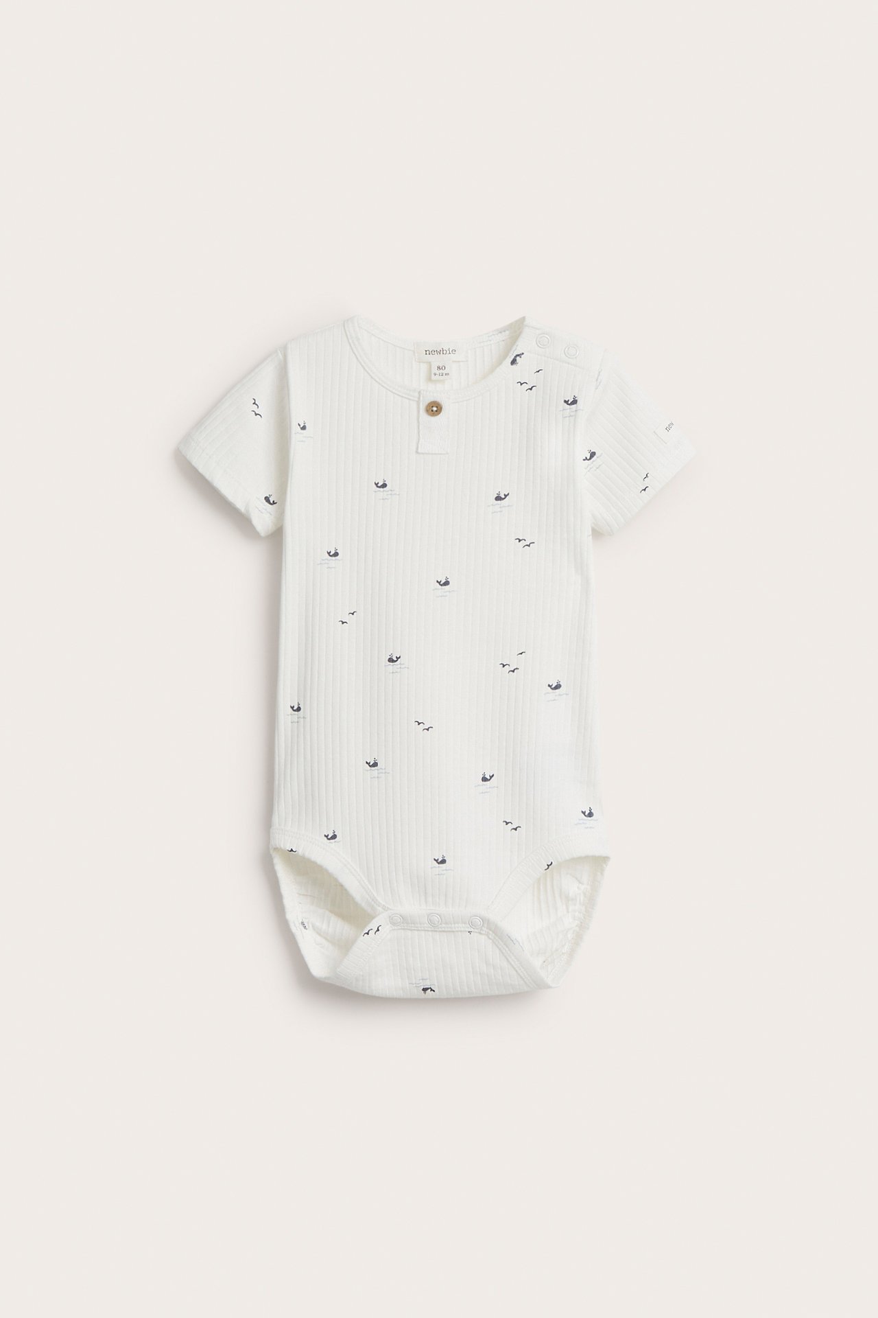 Frontvisning av en offwhite ribbet babybody med korte ermer, sjødyrmønster og trykknapper.