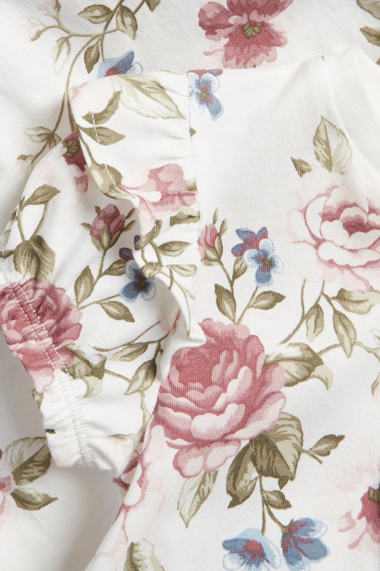 Närbild av en offwhite babypyjamas med rosa och blått blommönster och en volangärm.