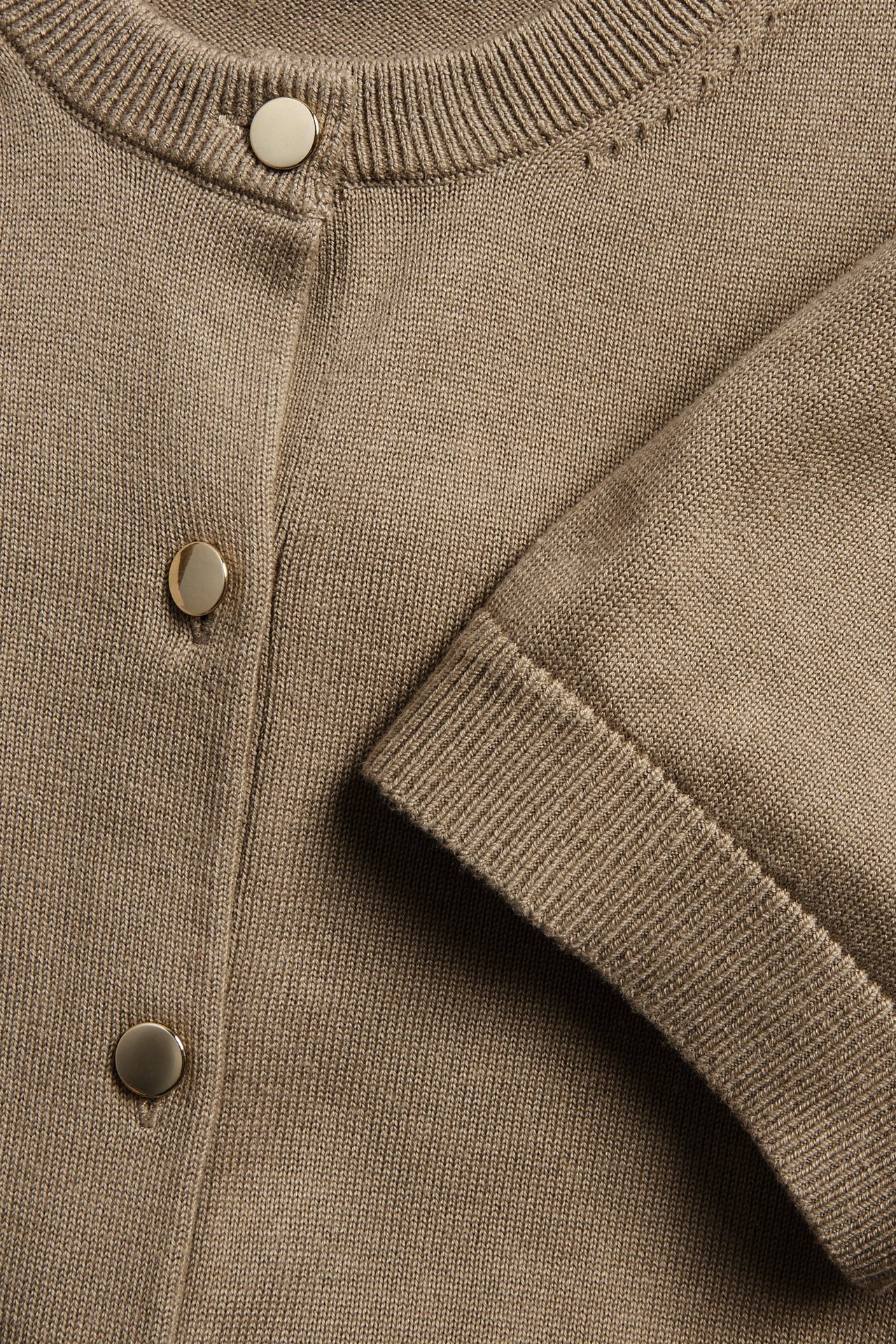 Zbliżenie na ciemnobeżowy, krótki kardigan z dzianiny, zapinany na złote guziki.
