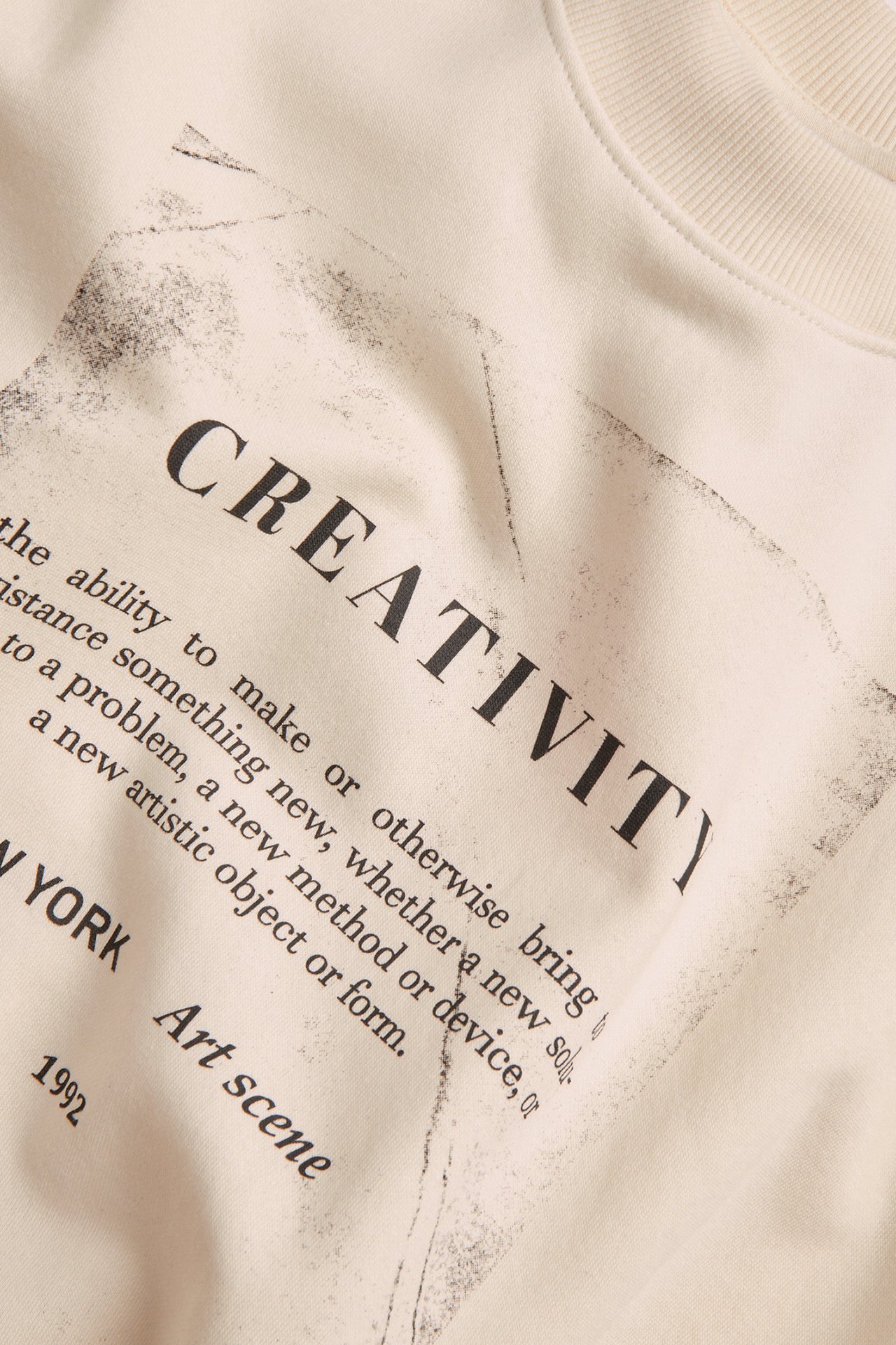 Nærbilde av en offwhite sweatshirt med svart 'CREATIVITY' teksttrykk foran.