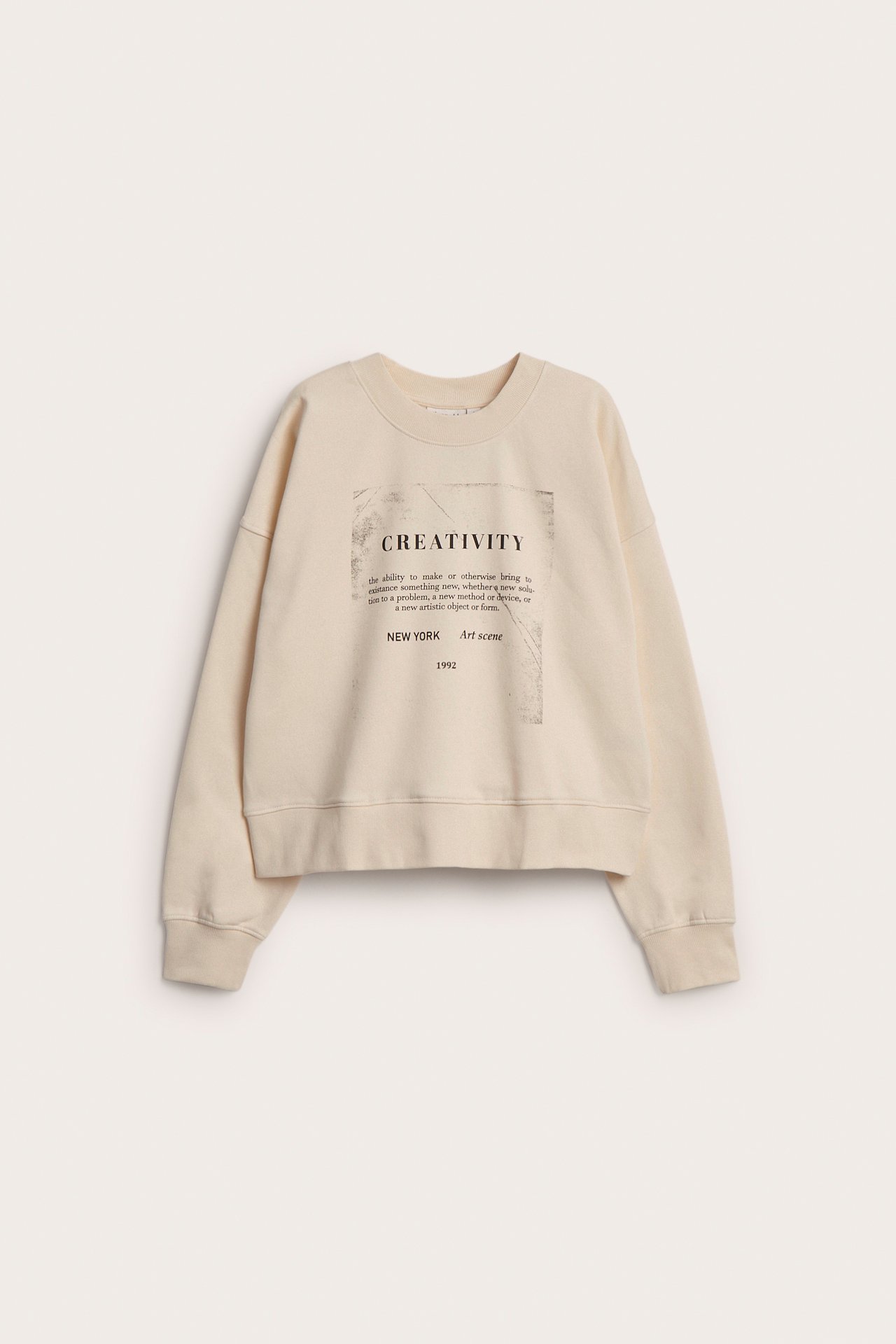 Frontvisning av en offwhite damegenser med "CREATIVITY"-teksttrykk foran.