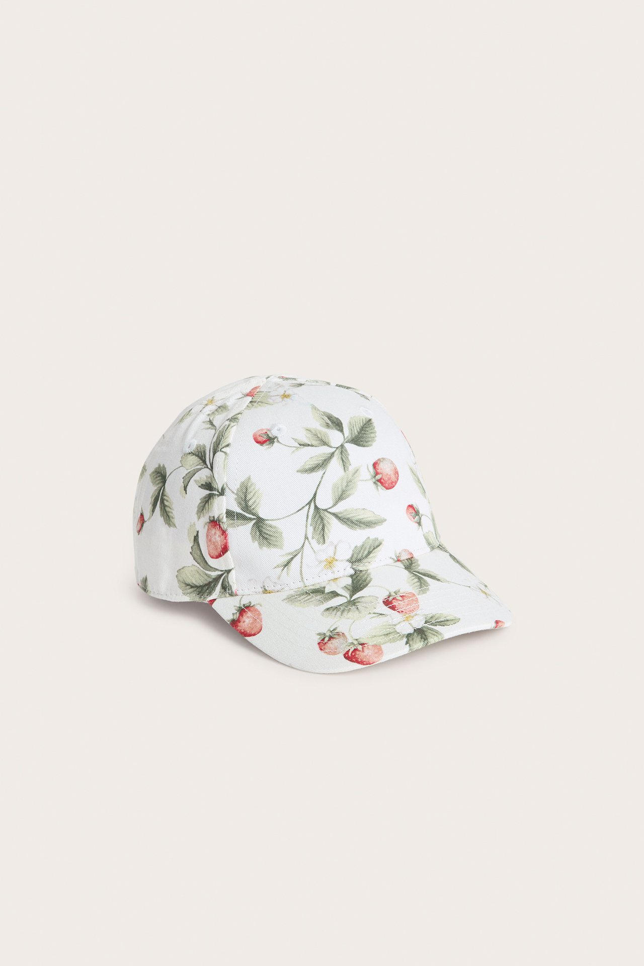 Skrå frontvisning av en offwhite baby-/barnekeps med rødt og grønt jordbærmønster.