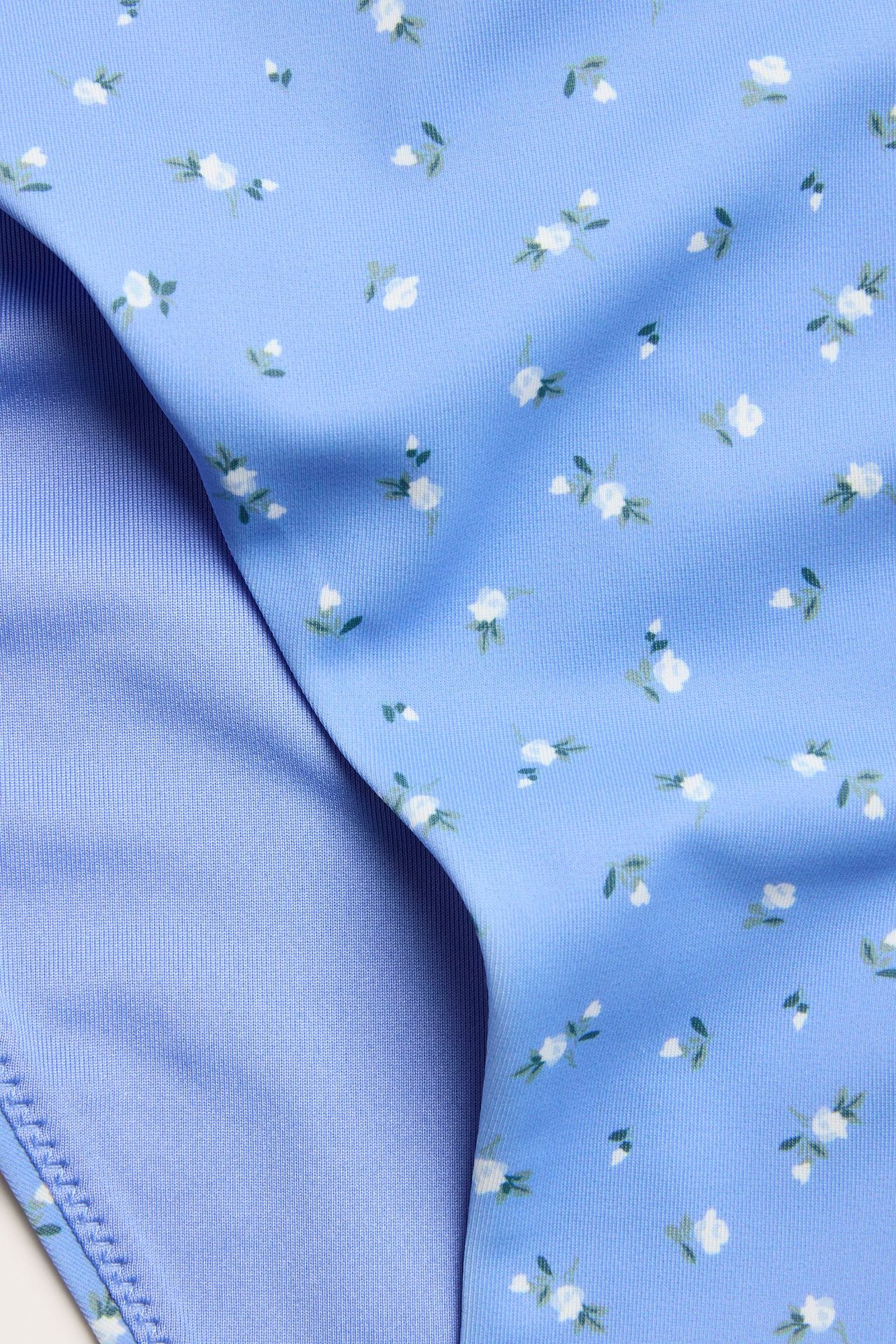 Zbliżenie niebieskich kwiecistych majtek bikini z białymi kwiatami i zielonymi liśćmi, widoczna niebieska podszewka.