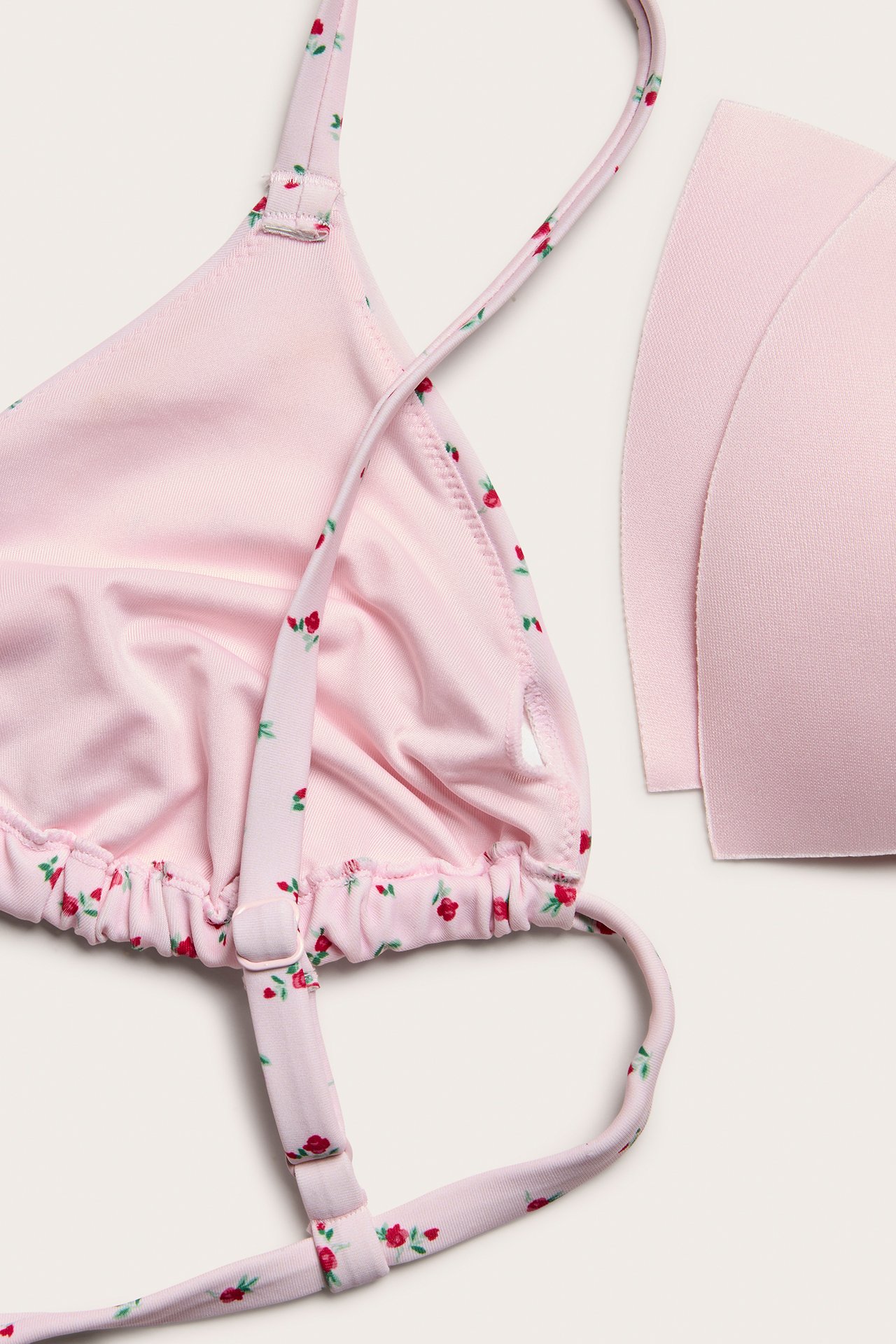 Zbliżenie na jasnoróżowy, kwiecisty biustonosz bikini z trójkątnymi miseczkami, regulowanymi ramiączkami i wyjmowanymi wkładkami.