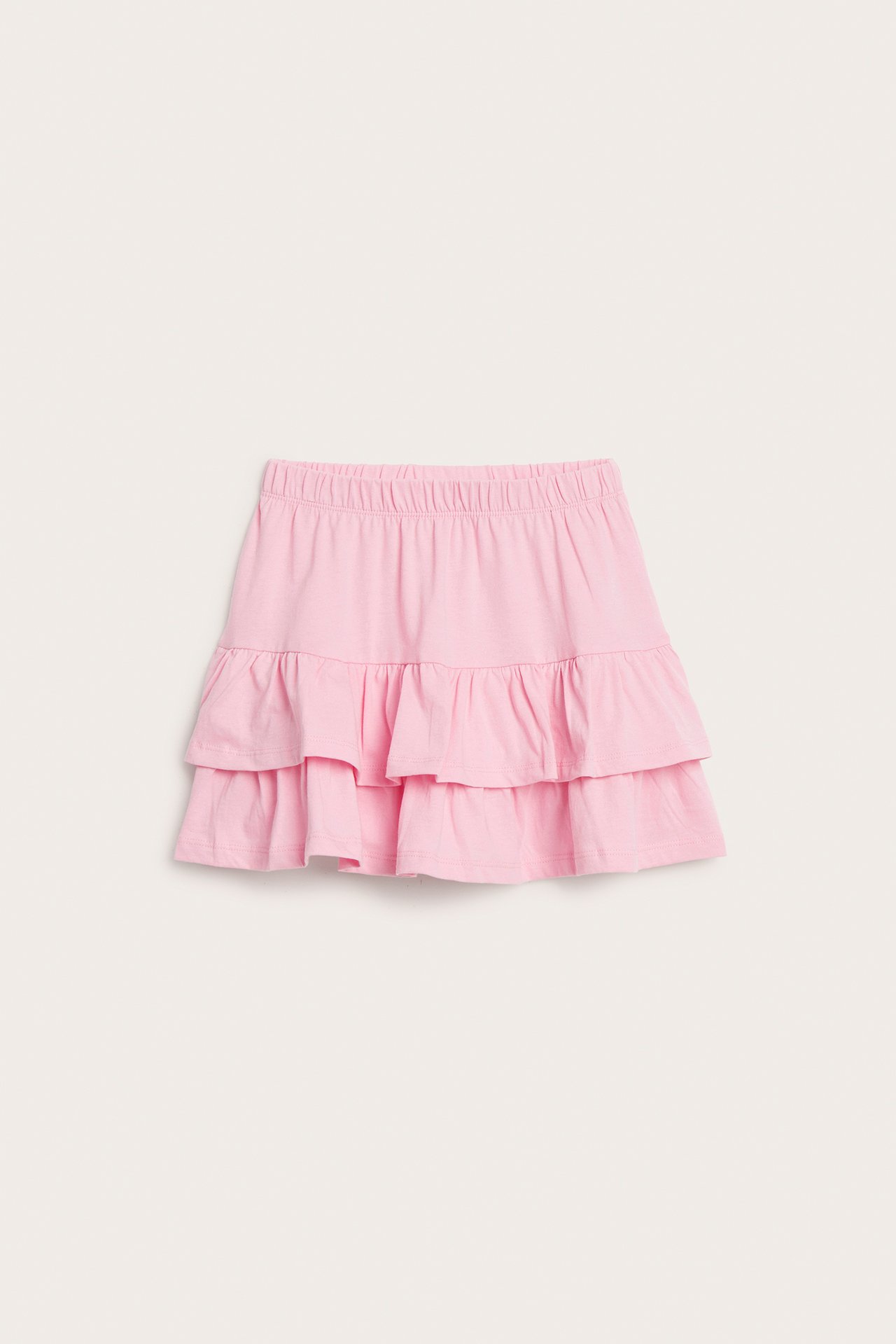 Frontvy av en rosa enfärgad volangkjol i trikå för barn med resår i midjan.
