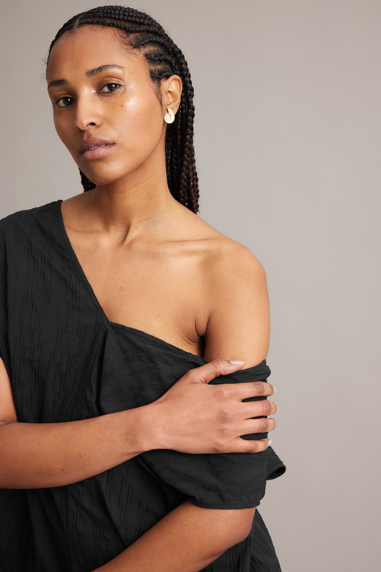Nærbilde forfra av en kvinne i svart krøllet off-shoulder kjole og hvite spiraløreringer.