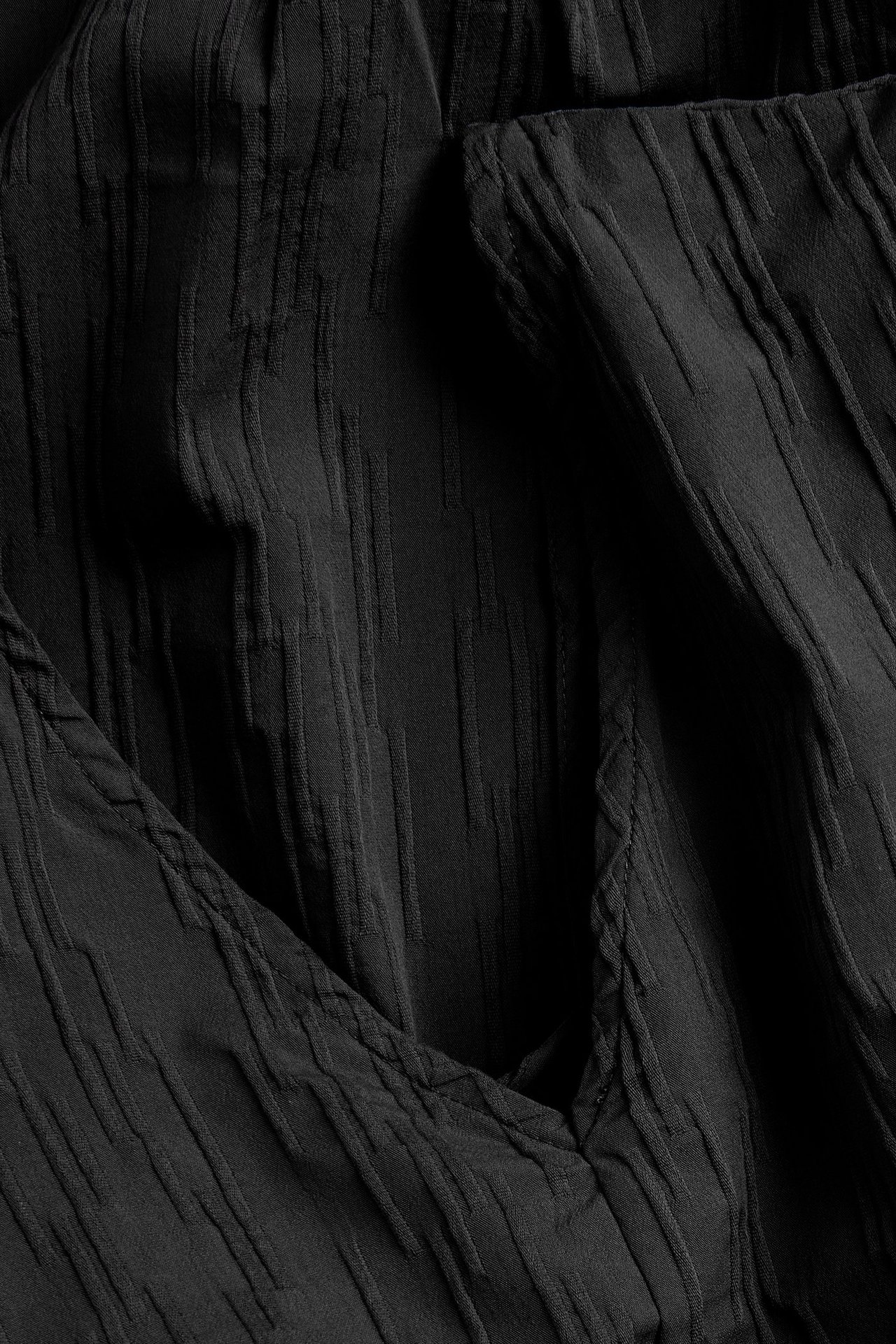 Zbliżenie czarnej, jednolitej, marszczonej sukienki z teksturowanym frędzlem.