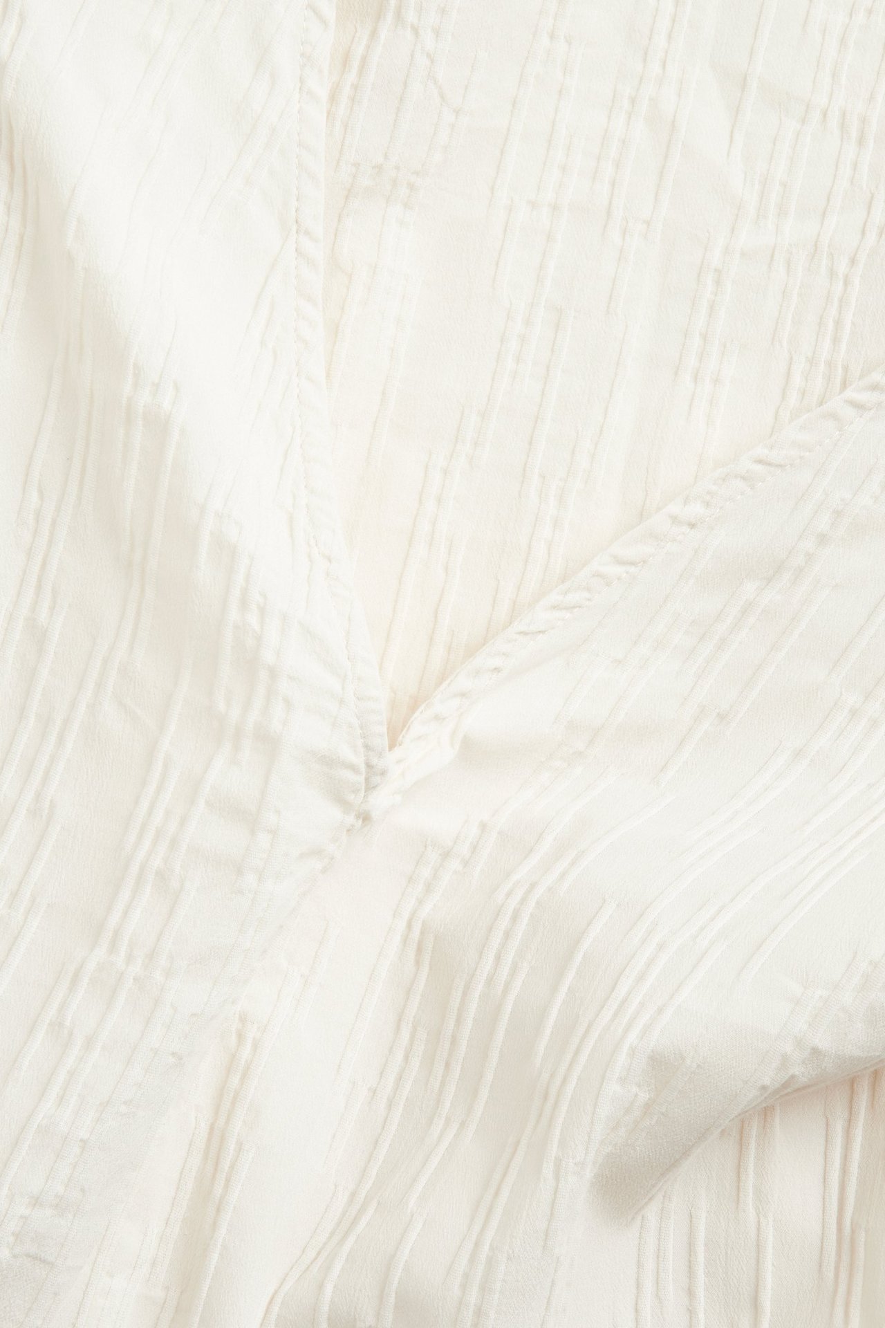Zbliżenie białej, marszczonej sukienki z mieszanki bawełny z dekoltem w serek i postrzępionym brzegiem.