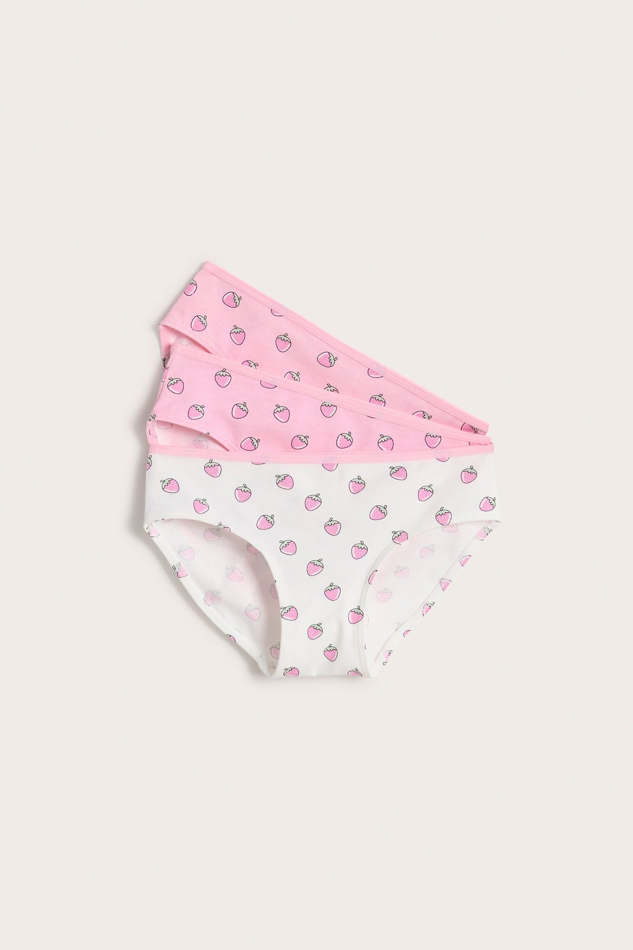 Ylhäältä näkymä kolmesta lasten puuvilla-alushoususta: yksi valkoinen, kaksi vaaleanpunaista, kaikki mansikkakuvioilla.