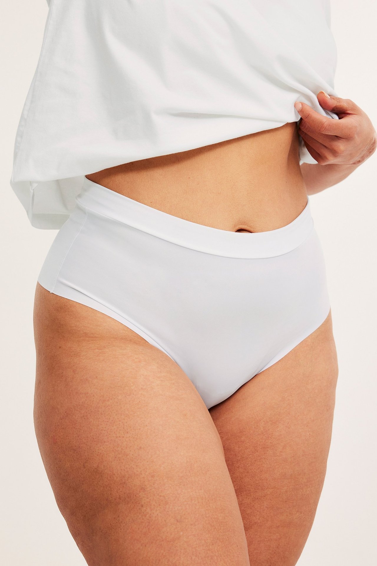 Zbliżenie z przodu na kobietę w białych, bezszwowych stringach z mikrofibry i białym T-shircie.