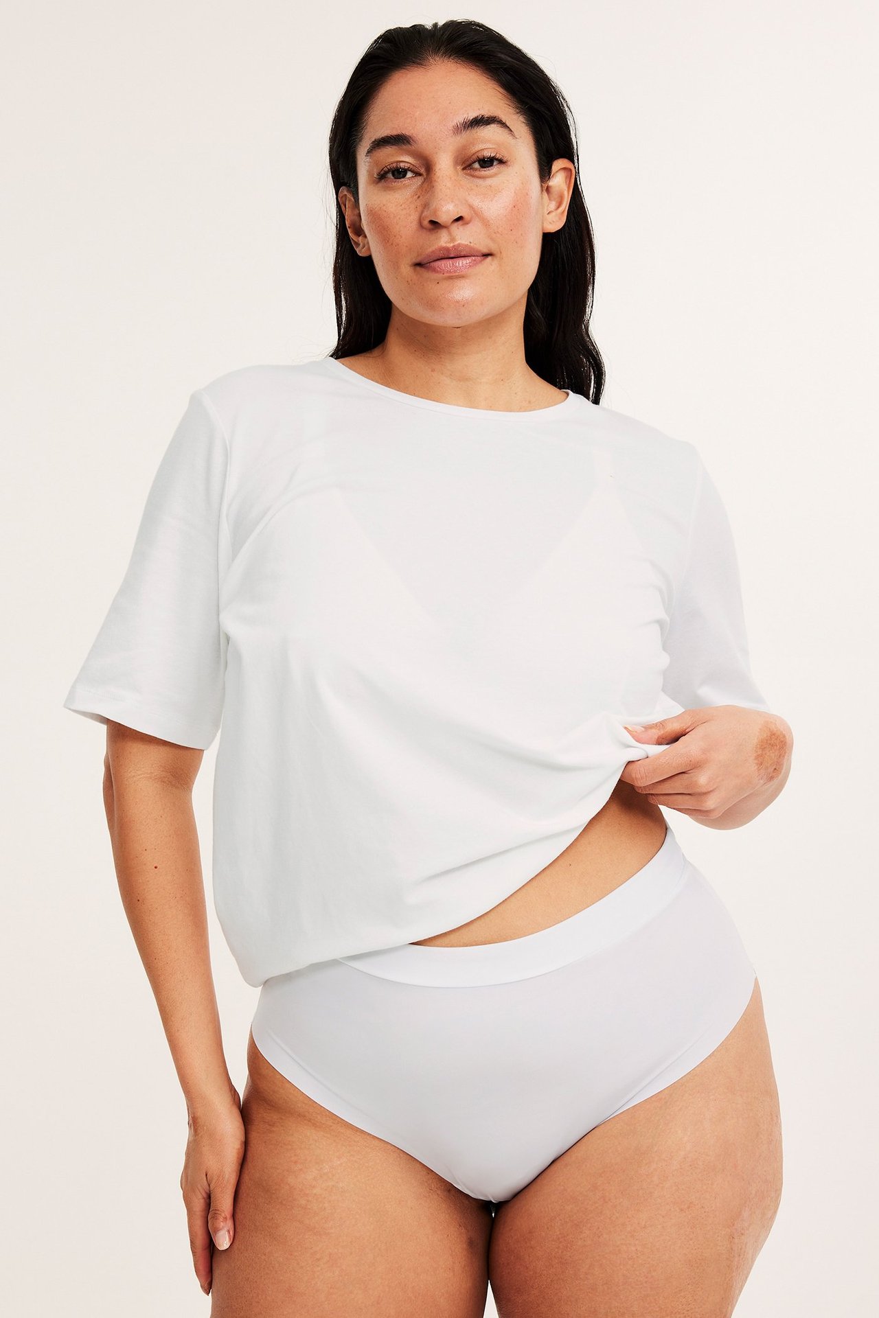 Forfra: kvinne i hvit mikro stringtruse med elastisk linning, under en hvit t-skjorte.