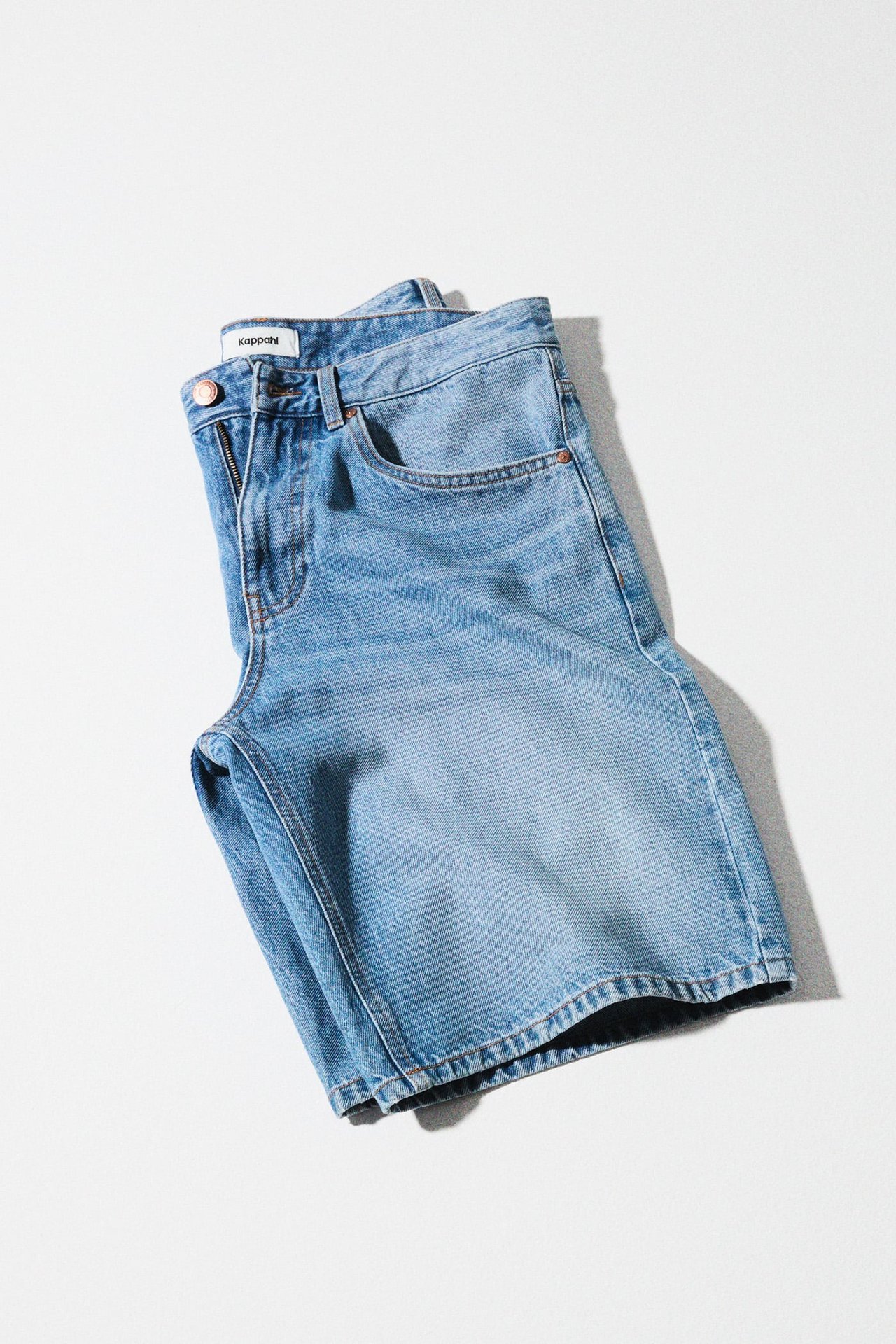 Uppifrån vy av vikta ljusblå denimshorts med en synlig kopparknapp.