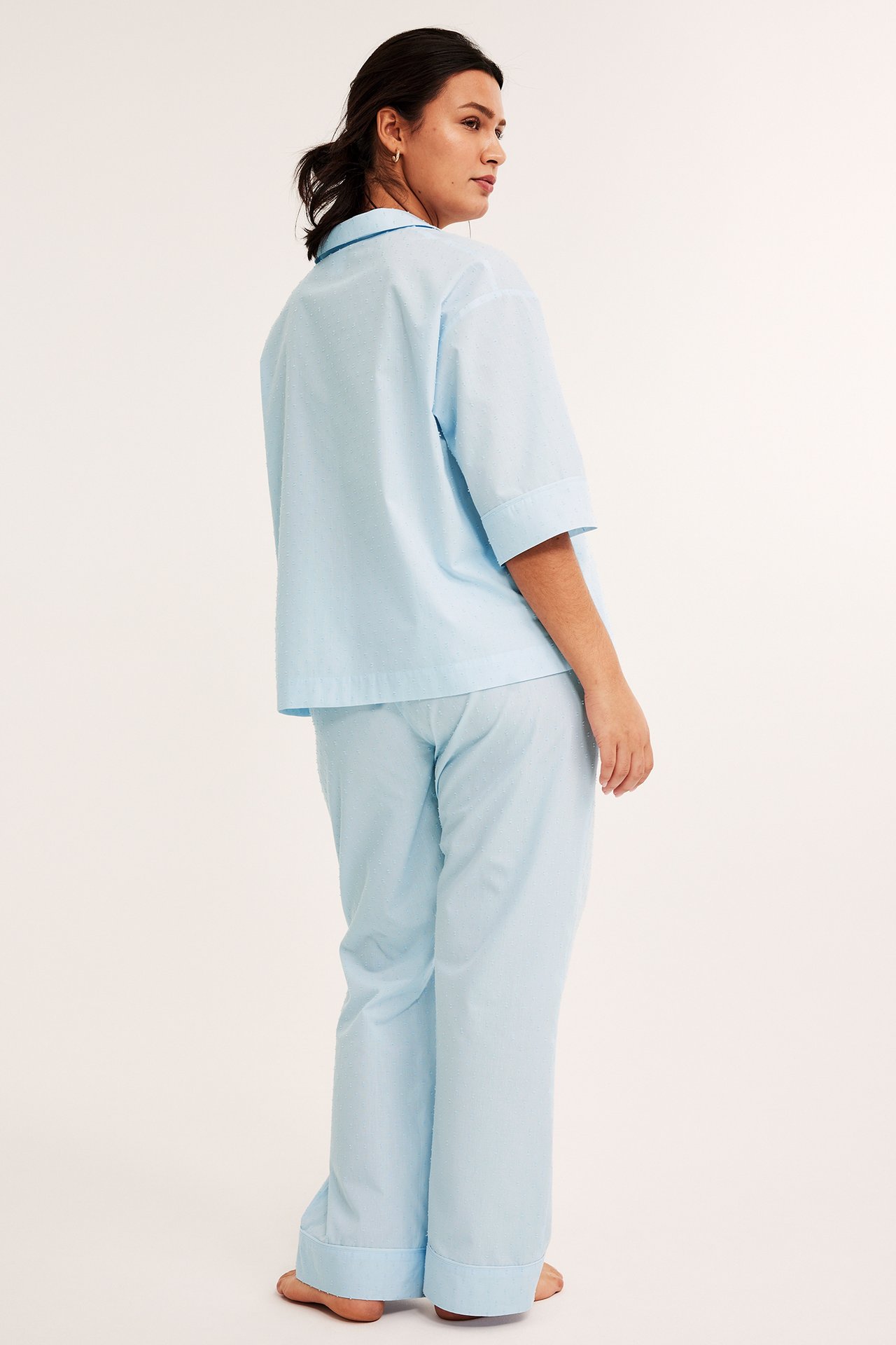 Naisen takasivukuva yllään vaaleansininen puuvillapyjama hienovaraisella ruutukuviolla.