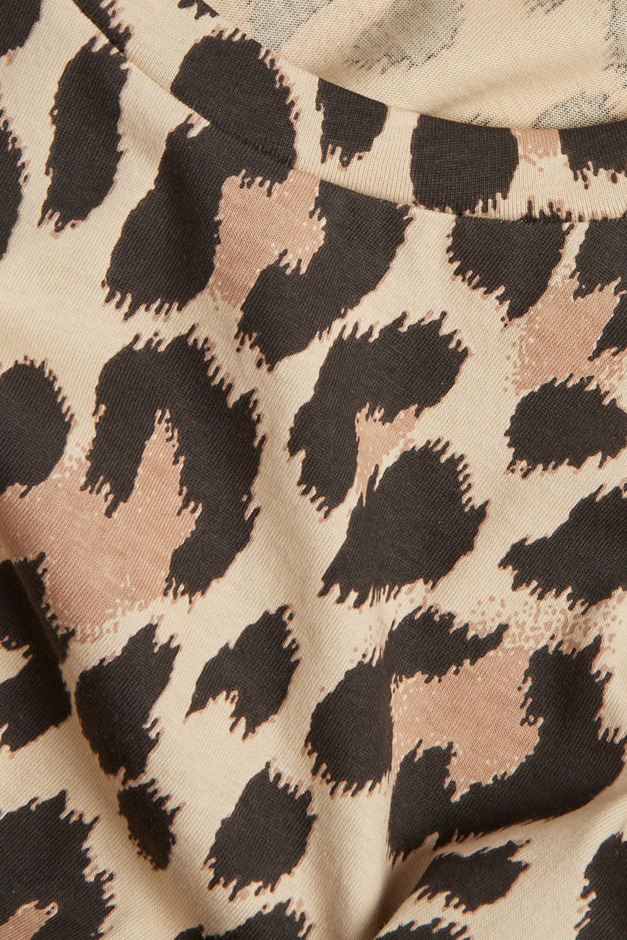 Nærbilde av en beige T-skjorte med mørkebrunt og lysebrunt leopardmønster, viser halslinningen.