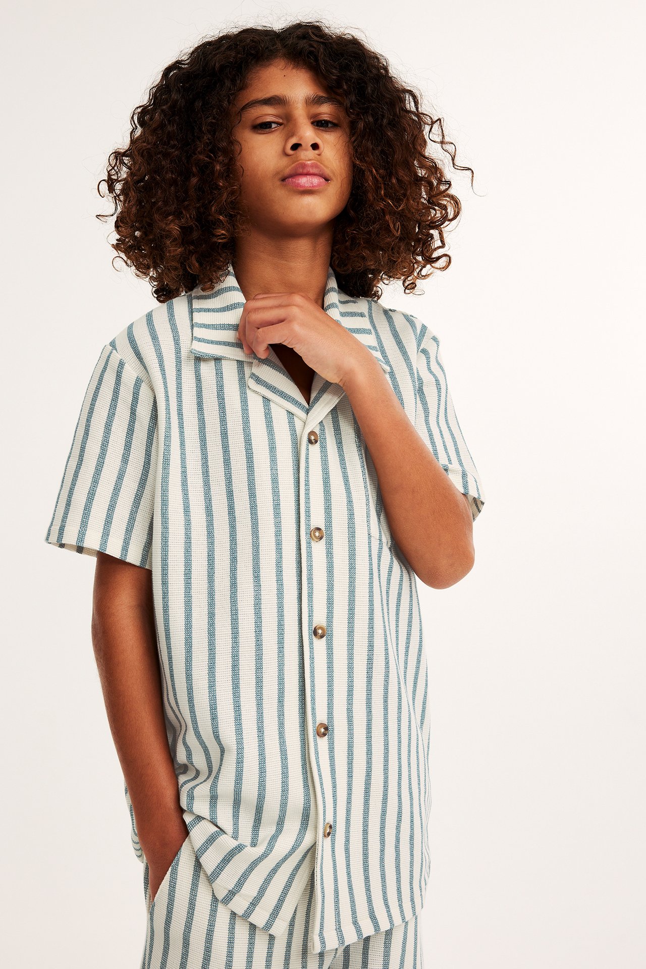 Frontvy av ett barn i offwhite och blårandig kortärmad skjorta med matchande shorts.