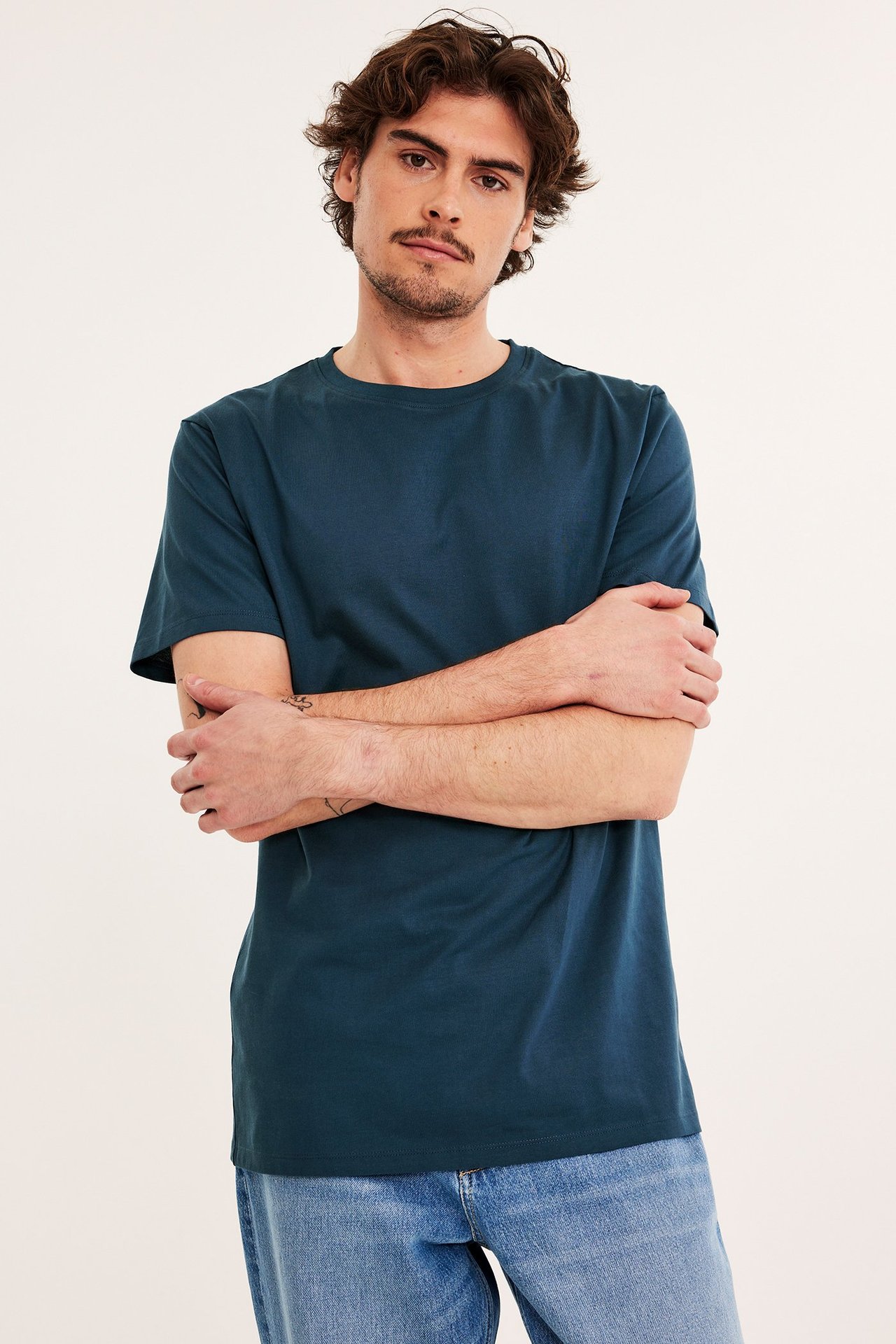 Edestä, mies tummansinisessä lyhythihaisessa puuvilla t-paidassa ja vaaleansinisissä farkuissa.