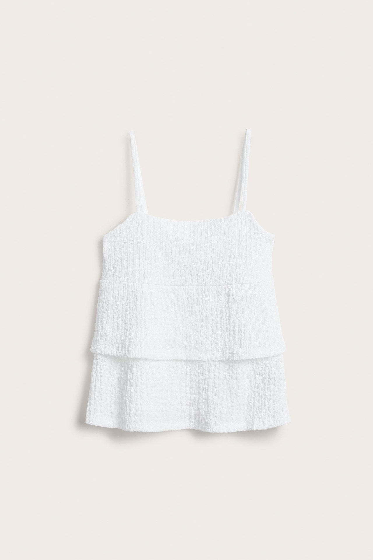 Framifrån, vit strukturerad jerseytopp med tunna axelband och volangdetaljer.